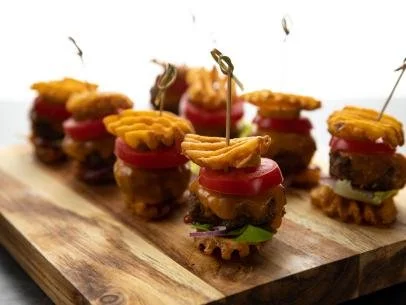 Gluten-free beef sliders with cheese, tomato and lettuce stacked between waffle fries.