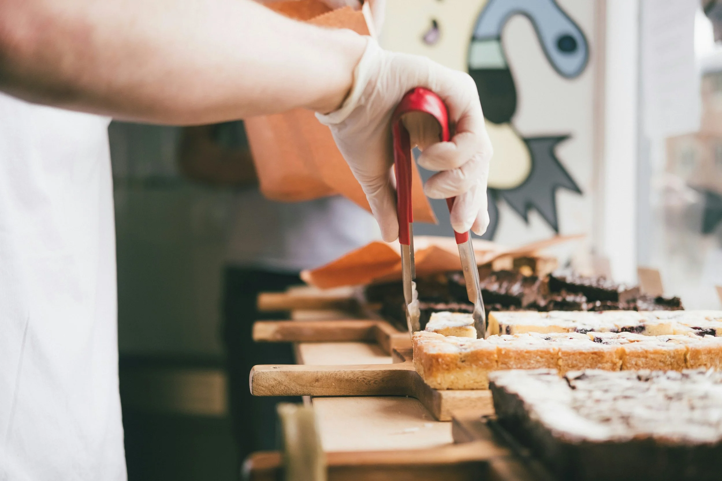 Person slicing fruit-filled dessert bars with kitchen tongs on wooden cutting boards, with a window and decorative wall art in the background.