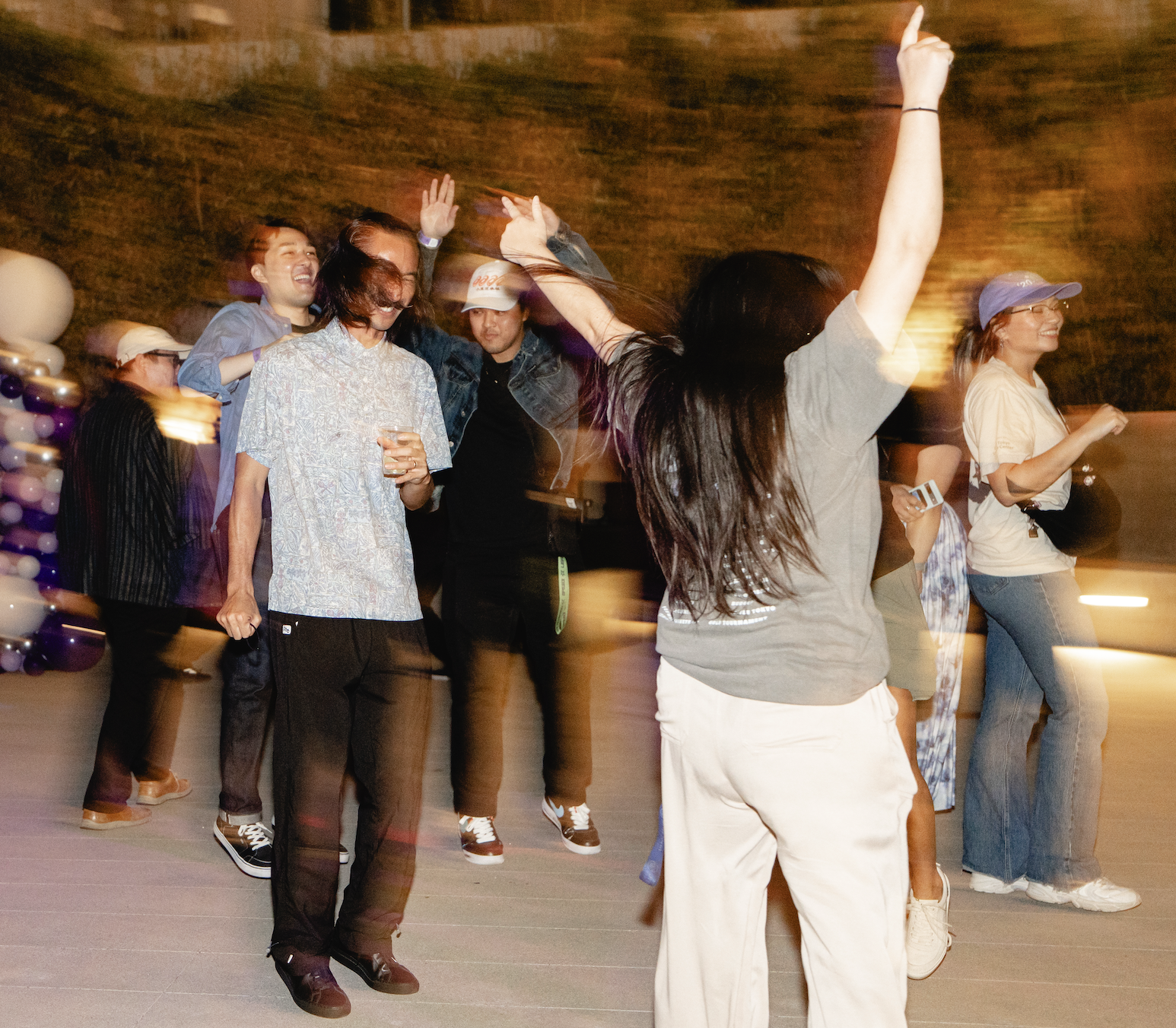 Group of young adults dancing and celebrating indoors, some smiling and raising their arms.