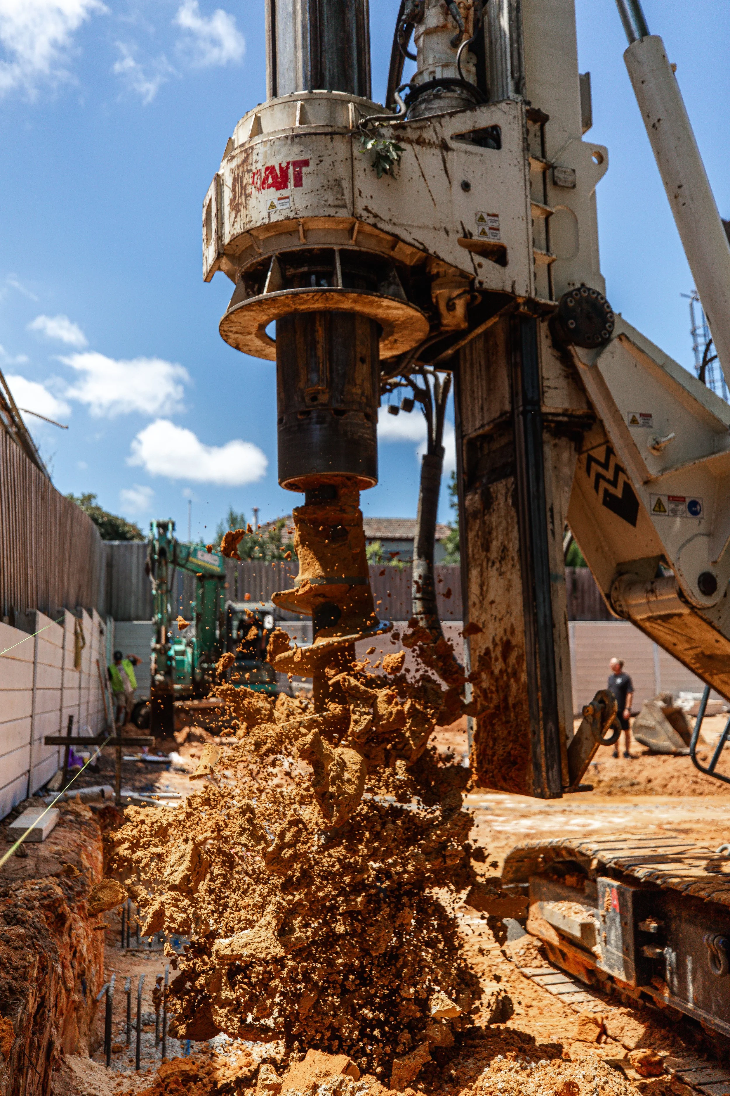 Close-up of an excavator's auger drilling into soil at a construction site on a sunny day.