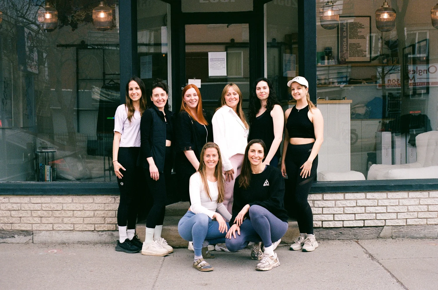 The Yoga D.N.A. team smiling together in front of the studio storefront on Masson street