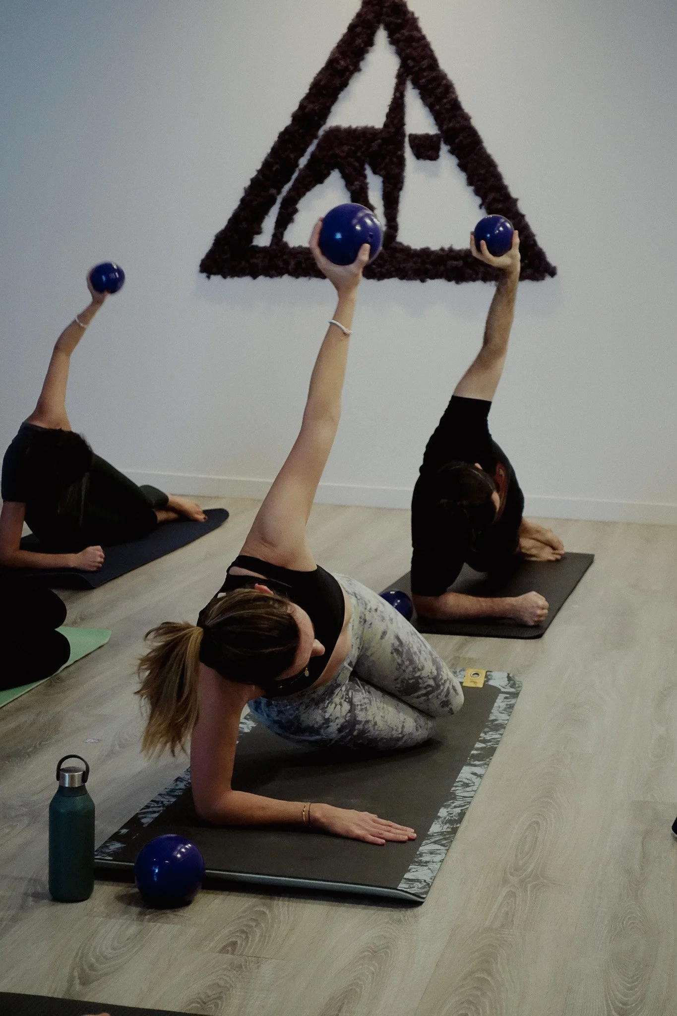 Women practising Pilates with small purple balls beneath the Yoga D.N.A. logo