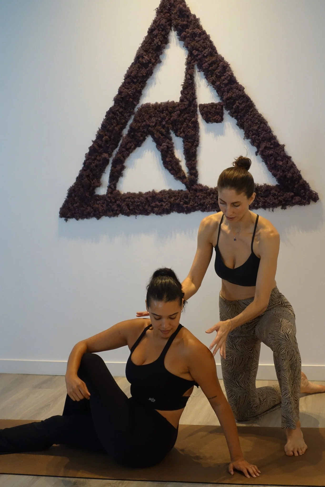 Instructor helping a client on a mat under the dried-flower Yoga D.N.A. logo