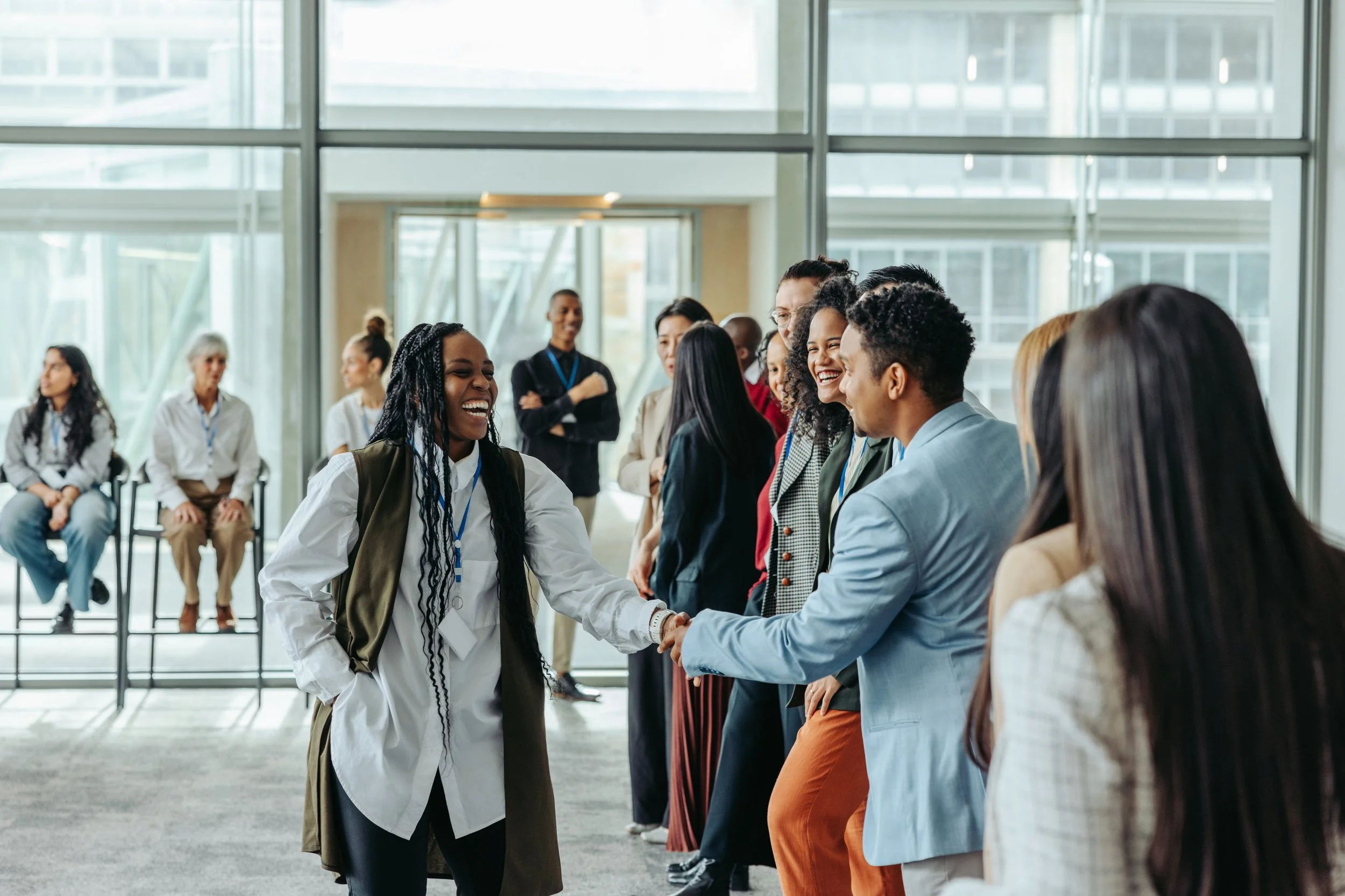 Group of diverse professionals greeting each other with handshakes and smiles in a modern office building.