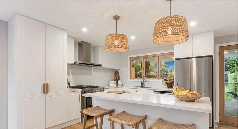 Modern kitchen with white cabinets, a large island with seating, stainless steel appliances, and woven pendant lights.