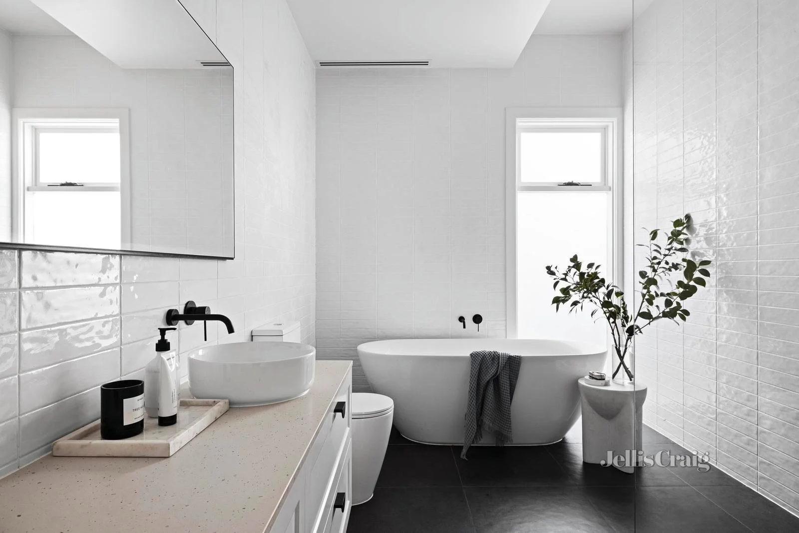 Modern white bathroom with a bathtub, vanity with a vessel sink, black fixtures, a large mirror, and a potted plant near the bathtub.