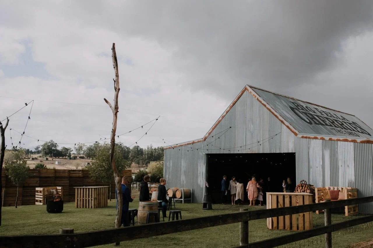 Modern house with a wooden deck, outdoor dining table, sliding glass doors, and a patio area with outdoor furniture, surrounded by a yard with fallen leaves and a black fence.