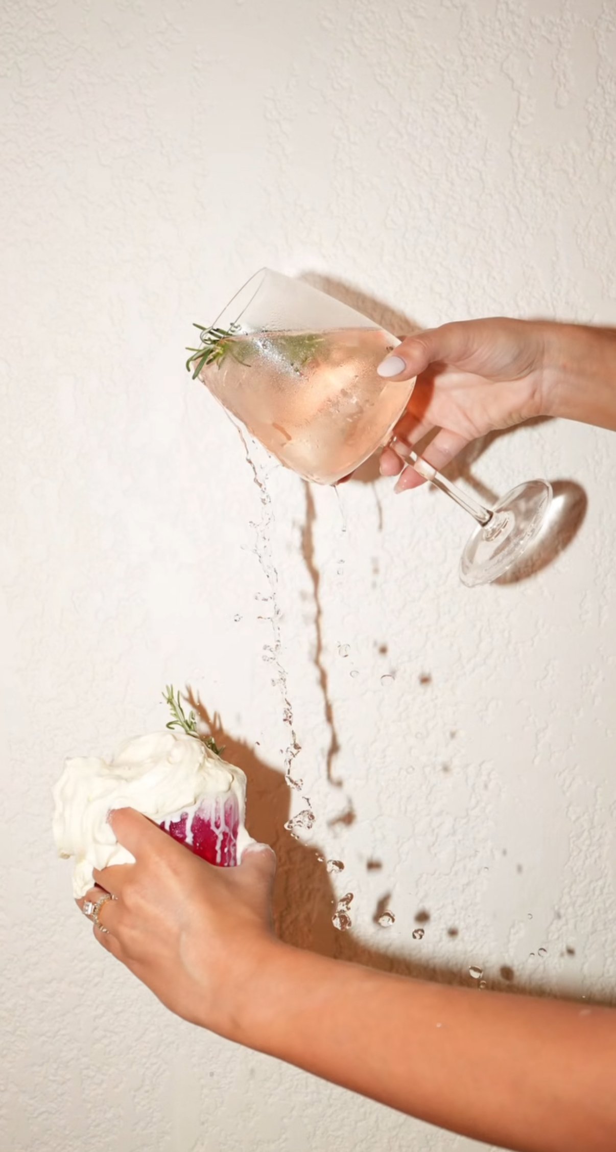 A person holding a wine glass spilling water onto a dessert, with a red and white cake in the background.