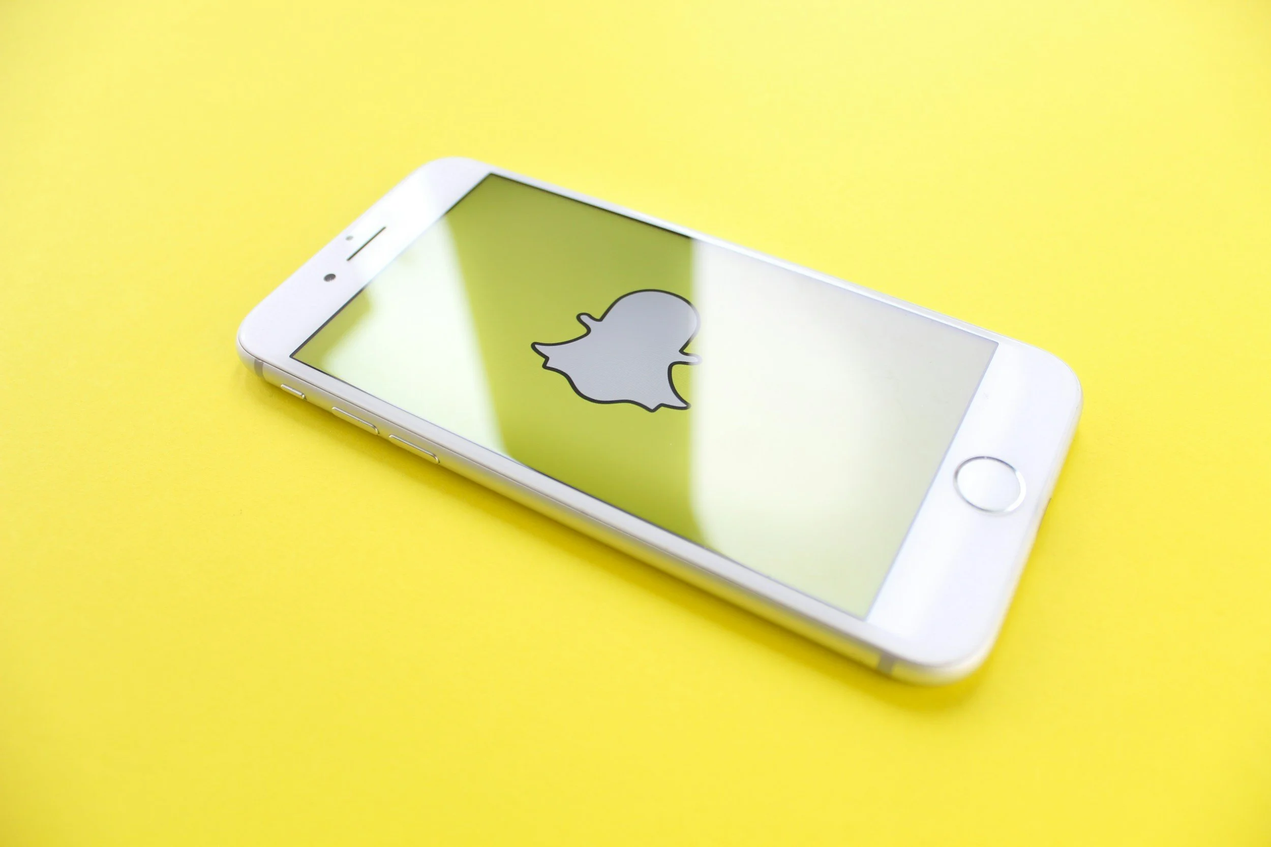A white smartphone with an Apple logo on the screen, resting on a yellow surface.