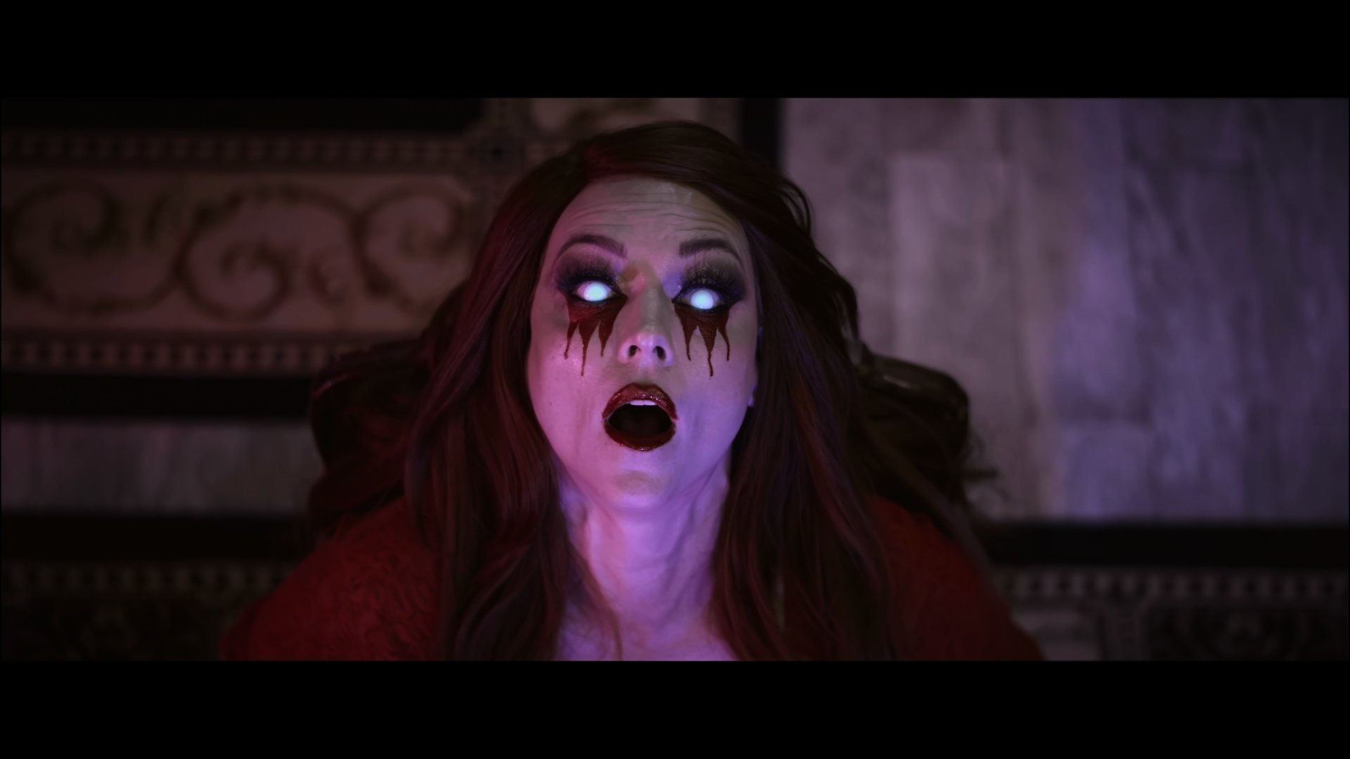 Close-up of Scarah with glowing eyes, dark makeup, and blood-like streaks down her face