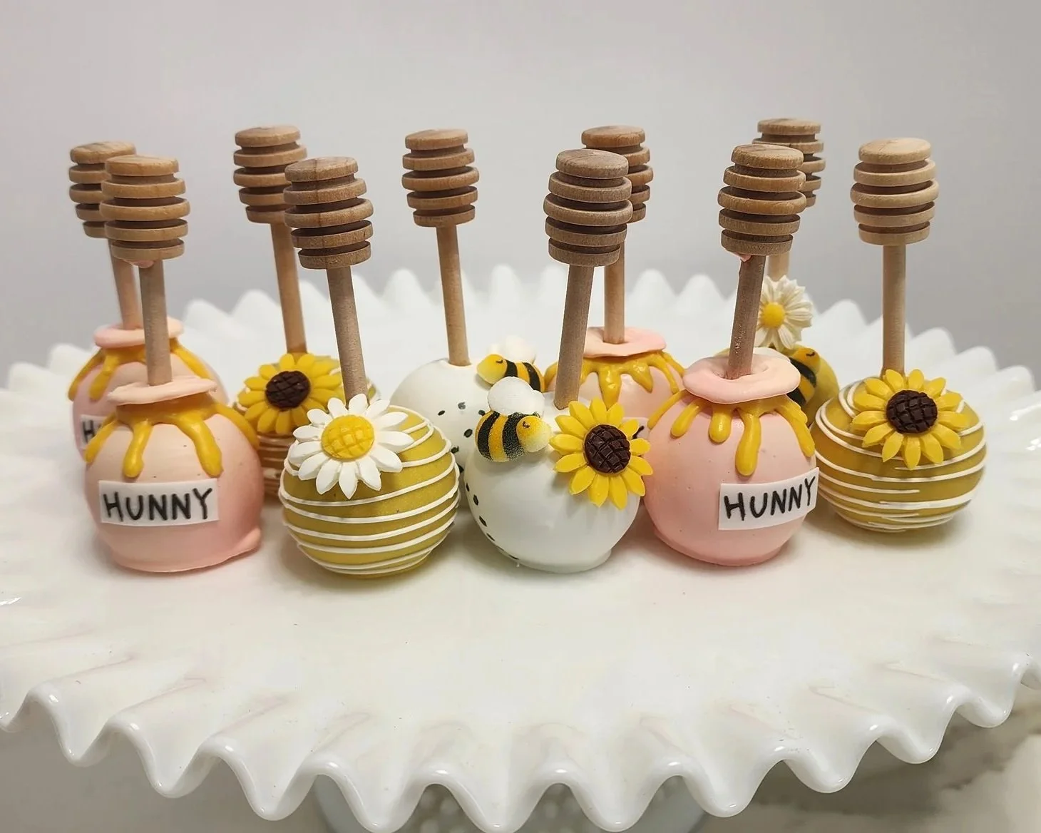 Decorative cake pops with honey, sunflower, and bee motifs displayed on a white plate.