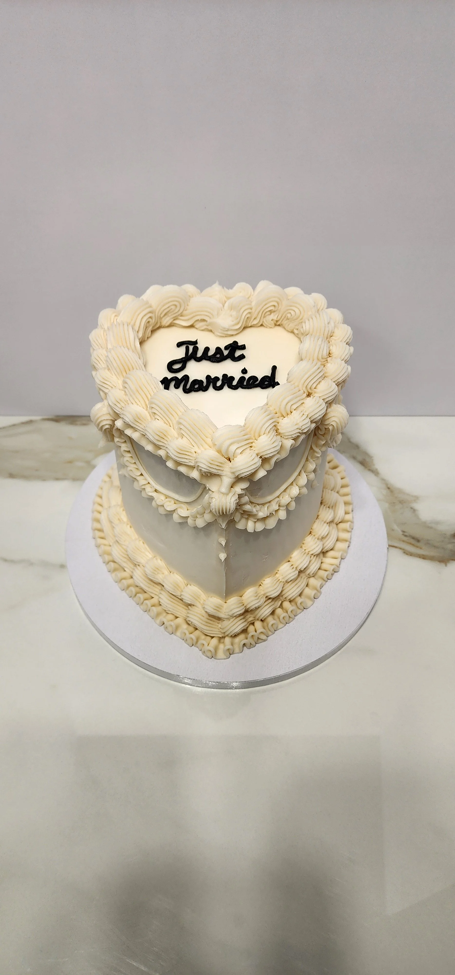 A white heart-shaped wedding cake with decorative piping, featuring the words "Just married" on top.