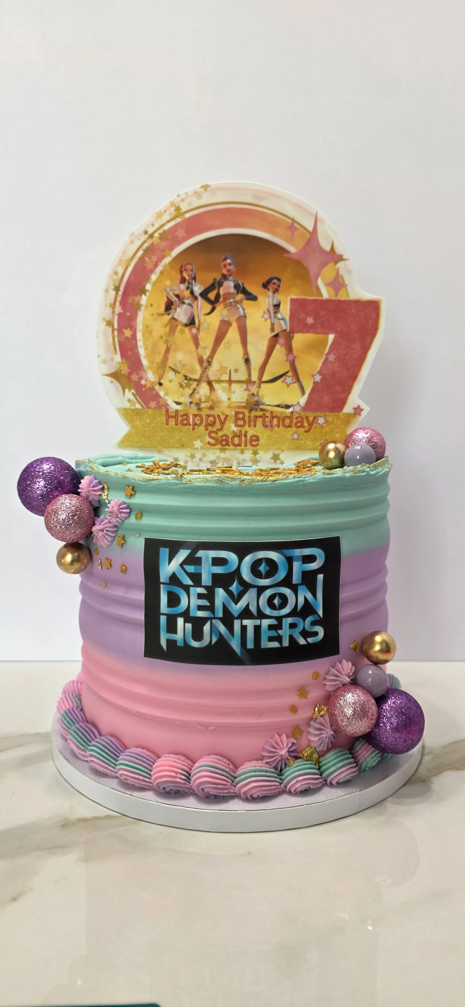 Colorful birthday cake decorated with glittery ornaments, pink, purple, and gold, with themed topper featuring the K-pop group Blackpink, personalized message 'Happy Birthday Sadie.'