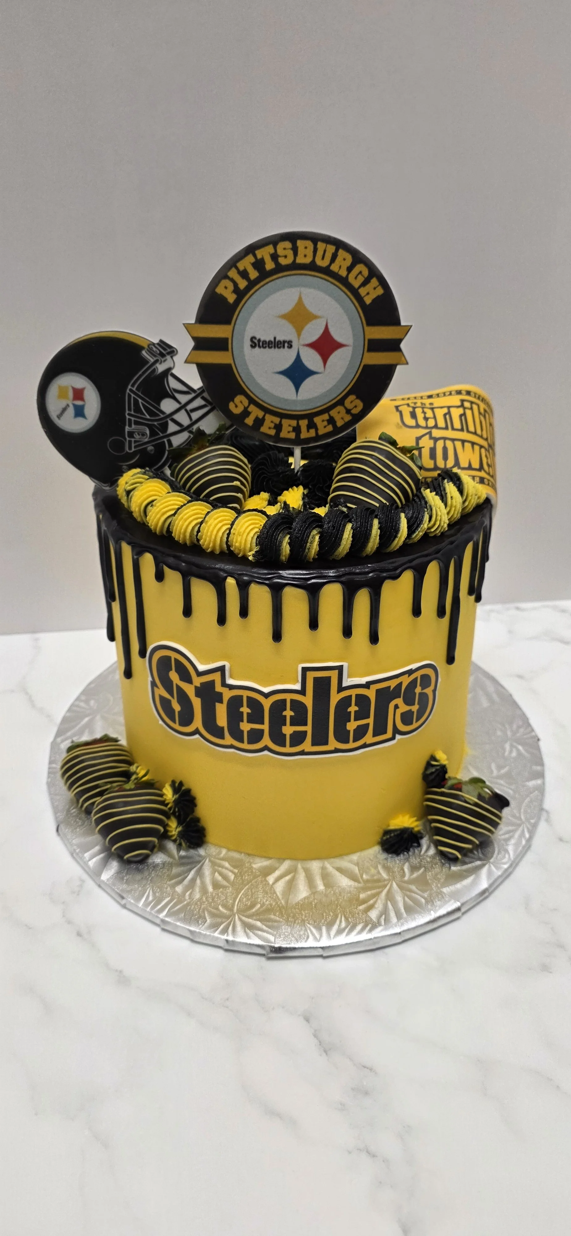 Yellow cake with black and yellow icing drip, decorated with chocolate and yellow icing, featuring Pittsburgh Steelers themed toppers and logos.