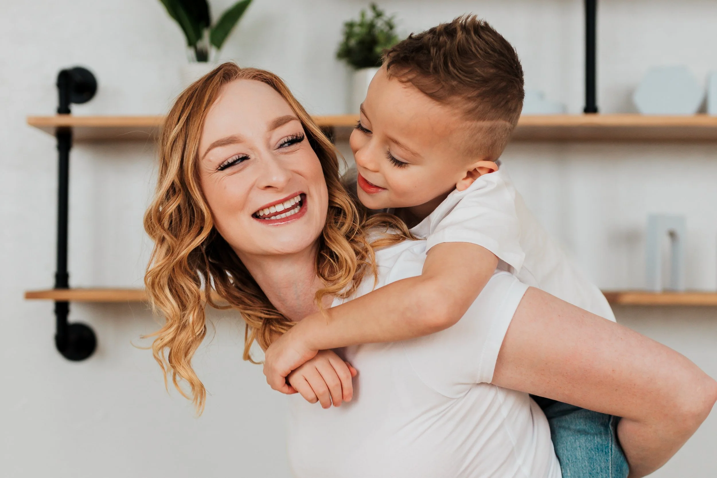 A woman with wavy red hair holding a young boy with short brown hair in her arms, both smiling and laughing.