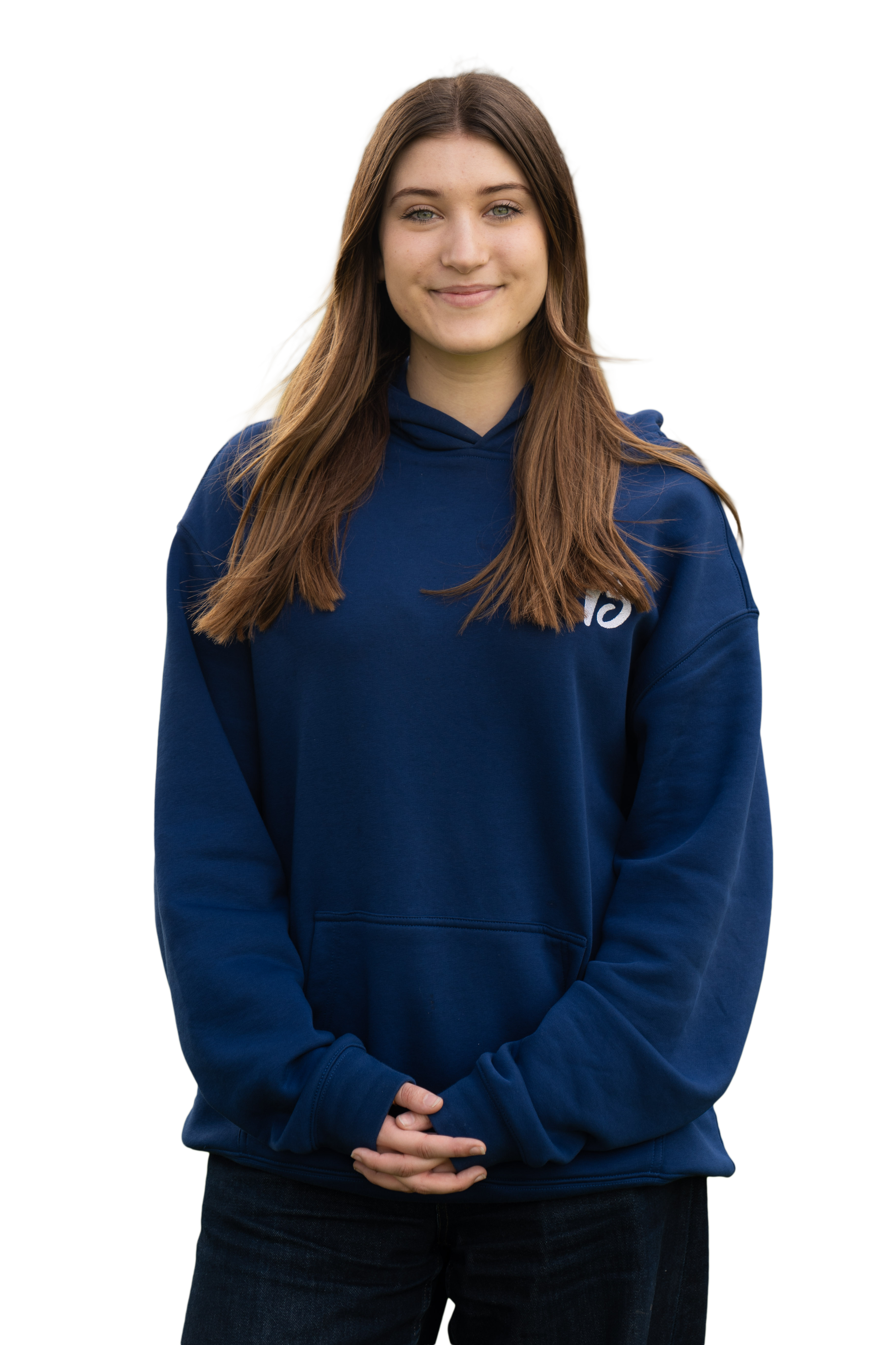 A young woman with long brown hair, wearing a navy blue hoodie, standing outdoors with her hands clasped in front of her, smiling softly.