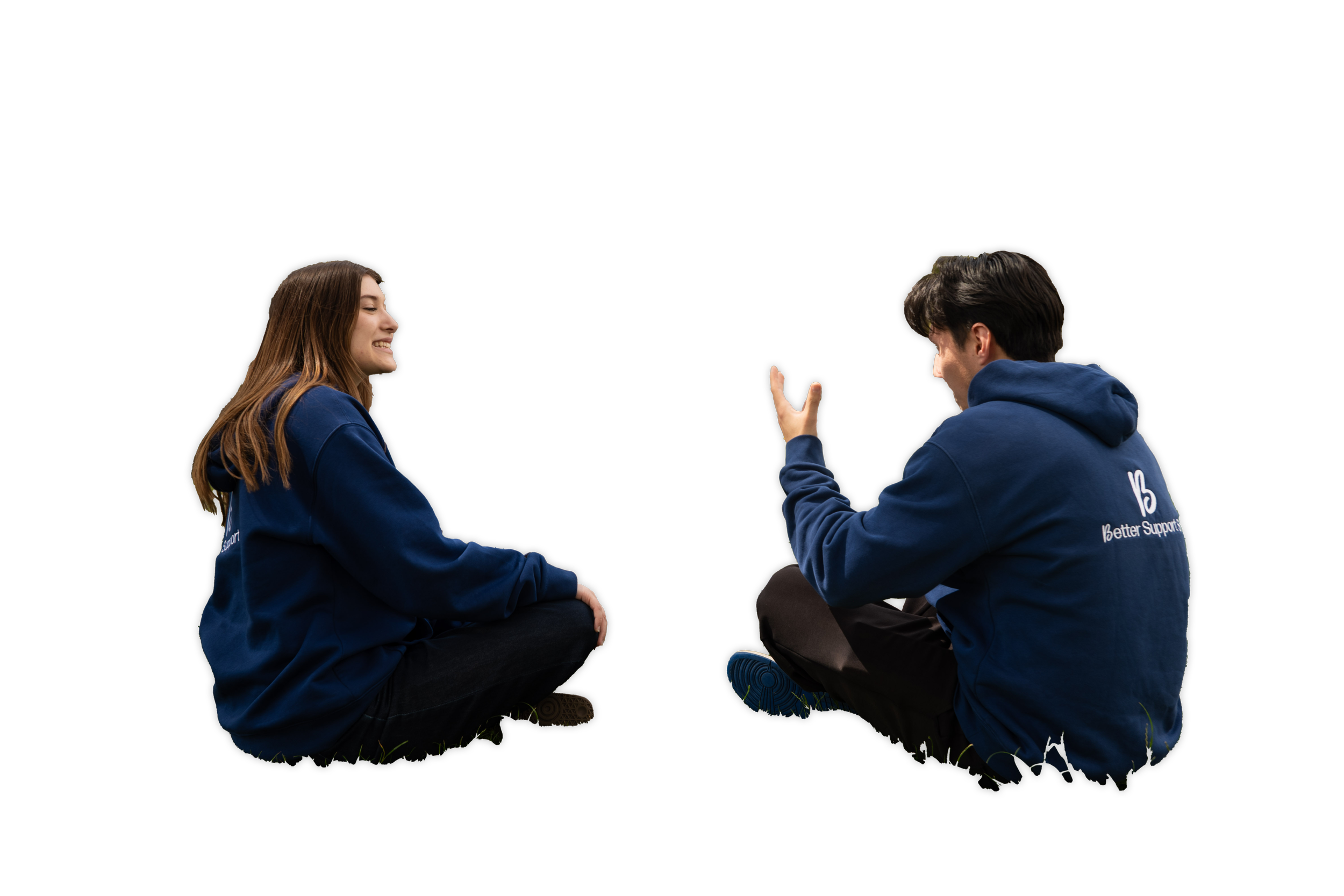 A young man and woman sitting cross-legged on grass against a black background, facing each other, smiling and engaging in conversation, both wearing blue hoodies.