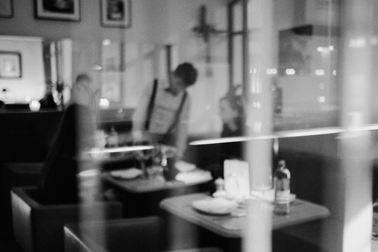 Blick durch eine Glasscheibe in ein Restaurant mit gedecktem Tisch im Vordergrund, im Hintergrund eine Person, die einen Rahmen hält, vermutlich bei der Arbeit.