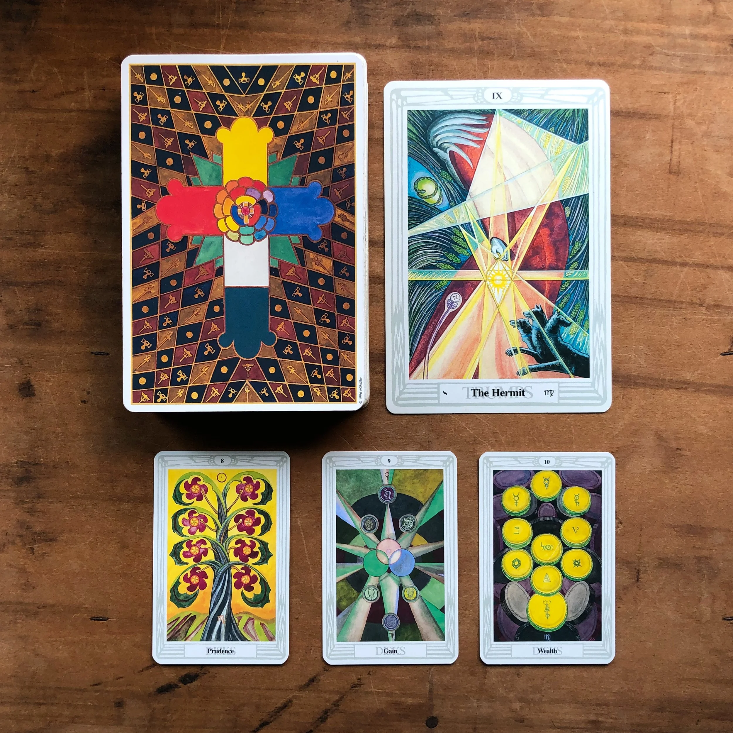 The Hermit card from the Thoth Tarot is pictured with its associated Minor Arcana cards, the 8, 9, and 10 of Disks.