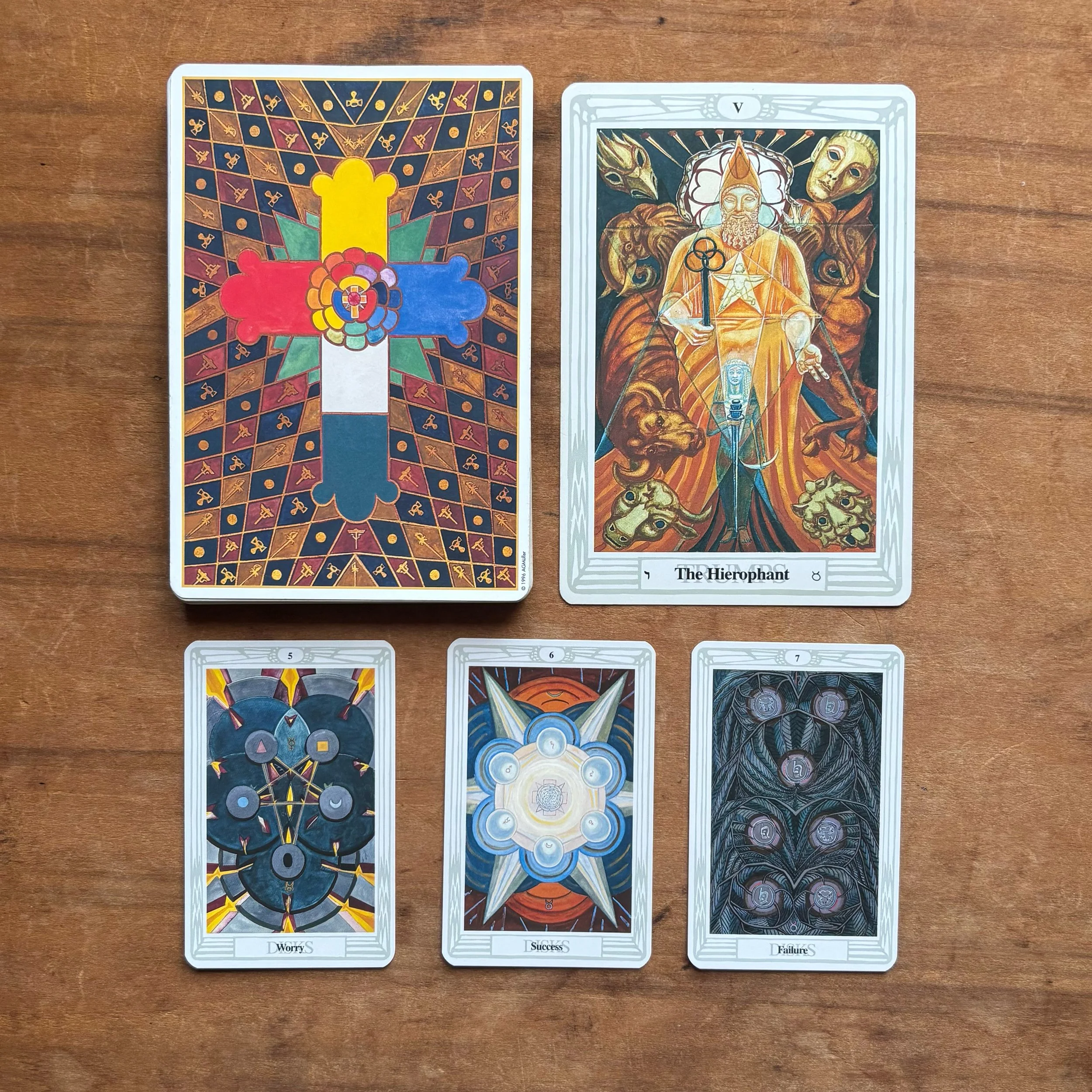 The Hierophant card from Crowley's Thoth Tarot is pictured with its associated Minor Arcana cards, the 5, 7, and 7 of Disks.