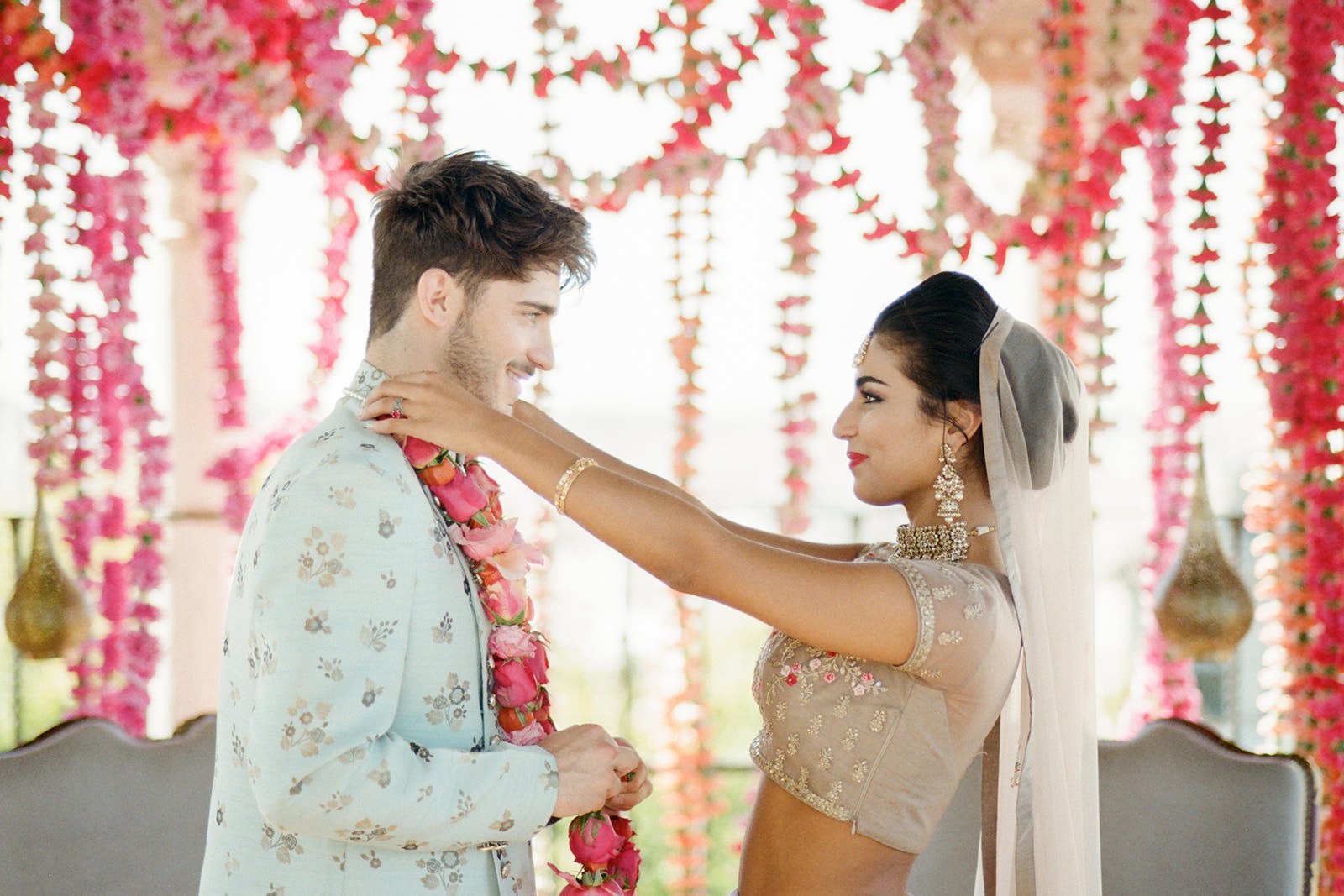 A couple exchanging flower garlands during a traditional ceremony with floral decorations in the background.