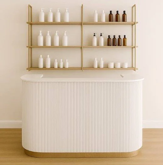 A white, ribbed counter with a rounded edge, set against a light-colored wall, with a wooden shelving unit above it holding white and brown bottles.