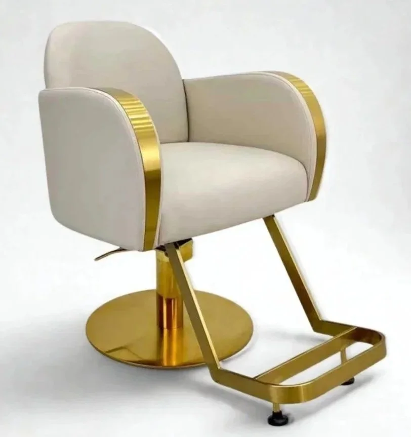 A modern salon chair with a white cushioned seat and backrest, gold-colored armrests, and a gold base with a footrest.