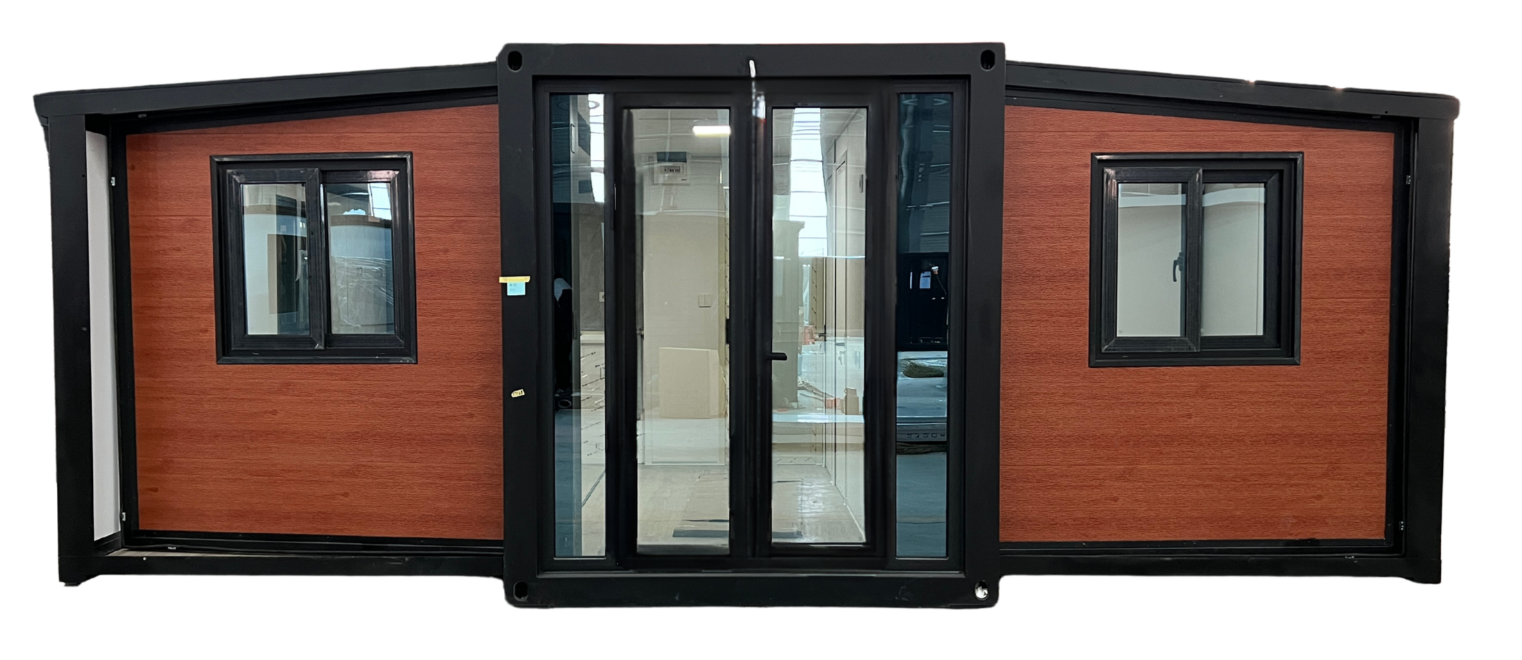 A small prefabricated building with wood panel exterior, black window frames, and glass doors, situated indoors.