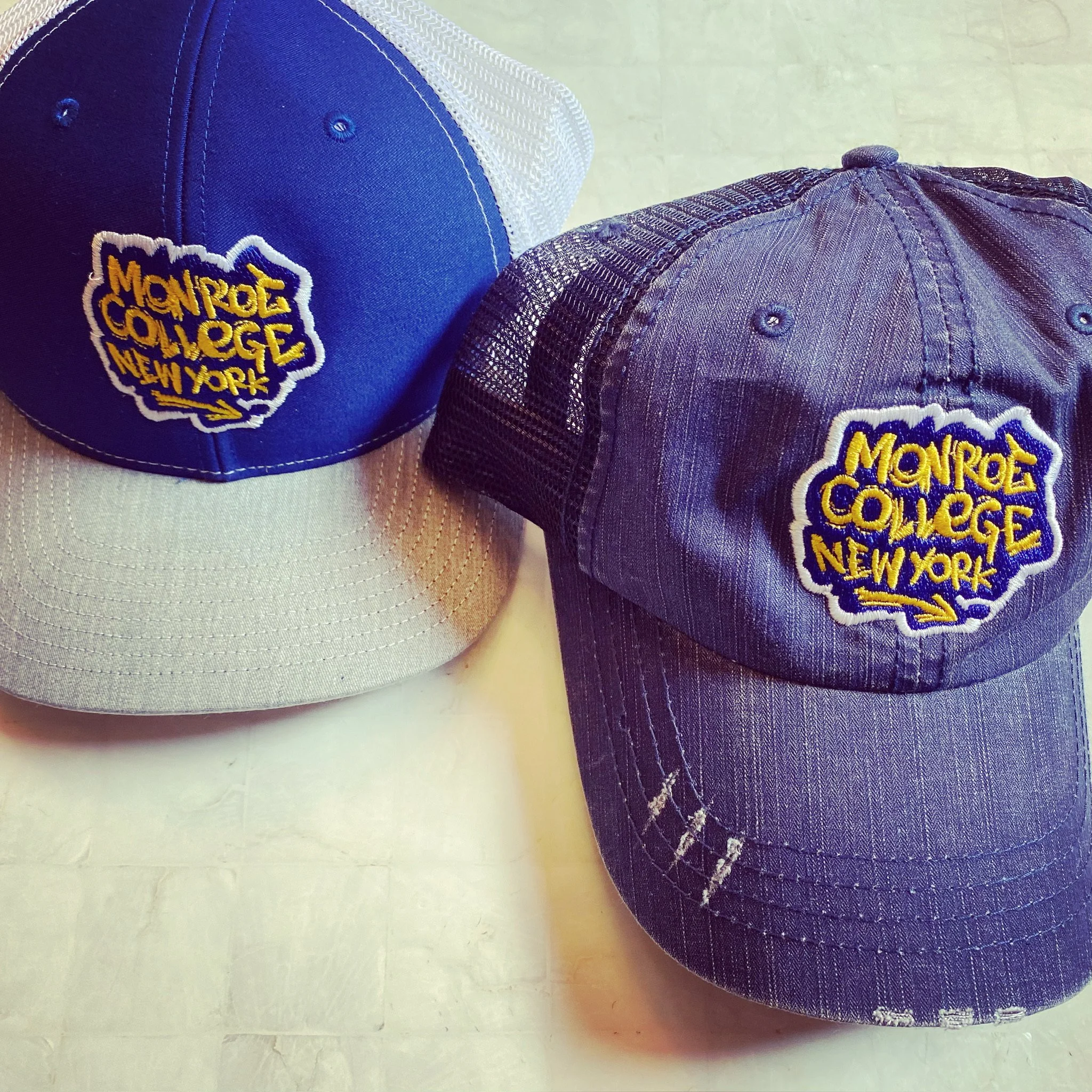 Two Monroe College branded caps in blue and gray