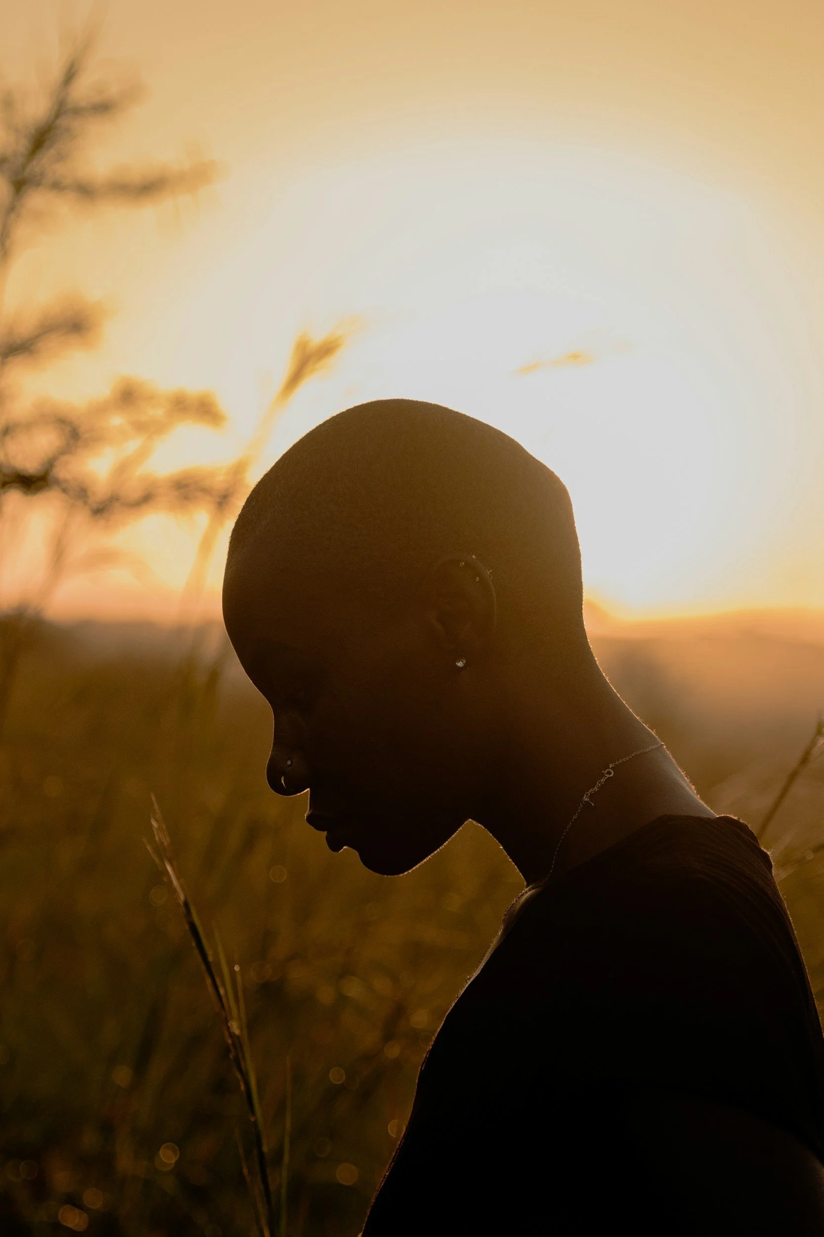 Woman in silhouette against golden sunset light, head bowed in quiet reflection