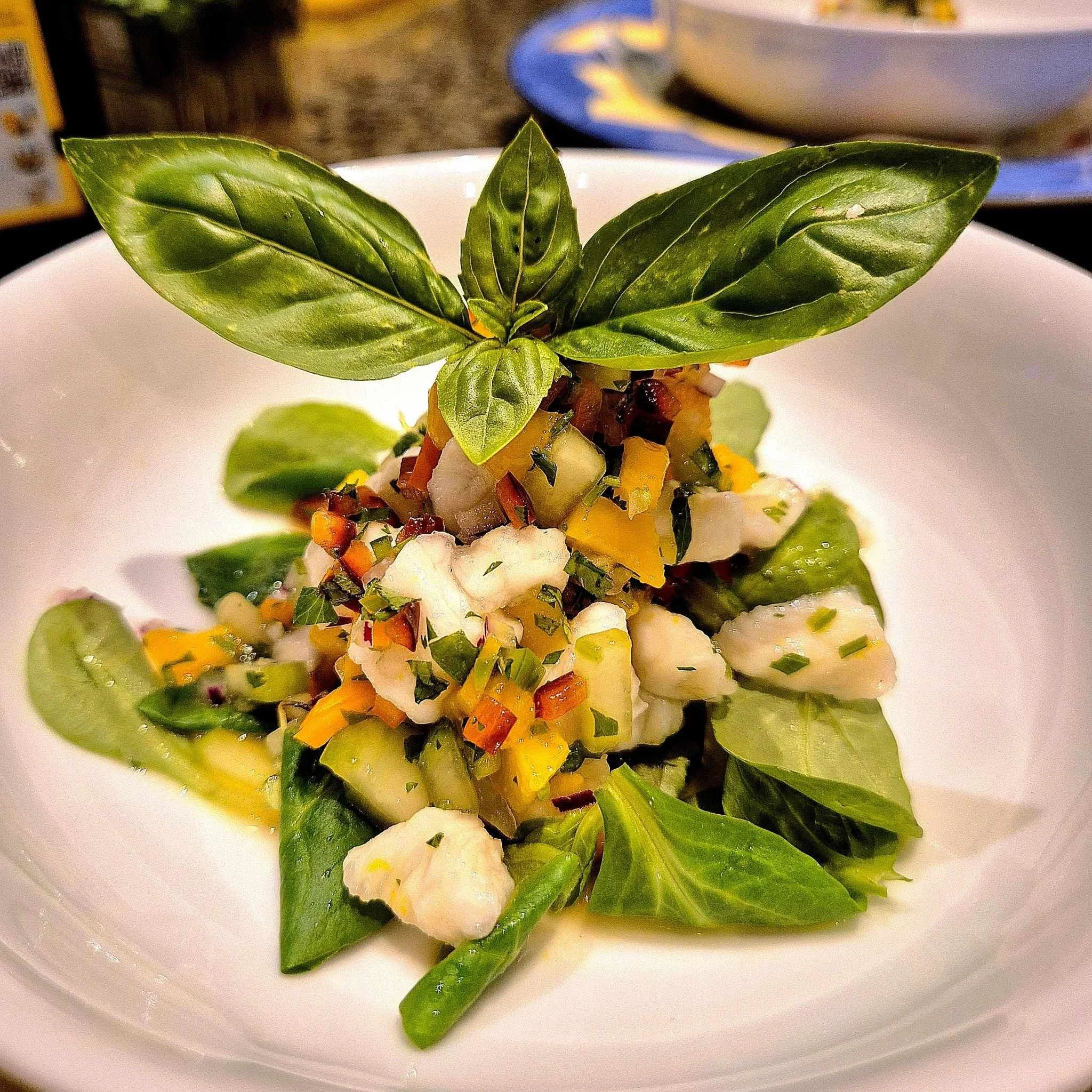 A dish featuring ceviche with diced vegetables, garnished with fresh basil leaves, presented on a white plate.