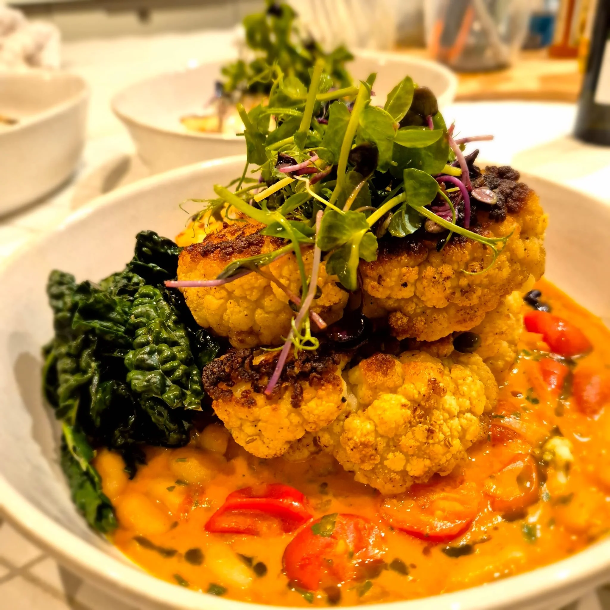 Close-up of a bowl with roasted cauliflower topped with microgreens, served over a bed of fragrant yellow curry with vegetables, including red peppers and greens.