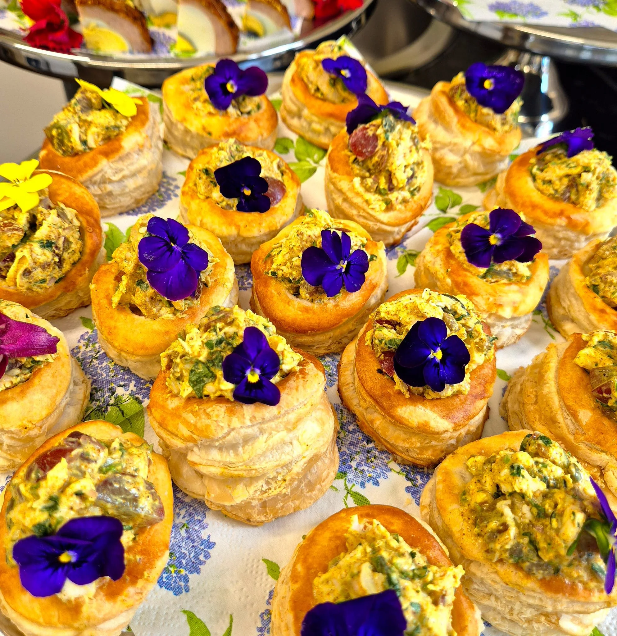 Variety of puff pastry bites topped with a spread, garnished with edible purple and yellow flowers.