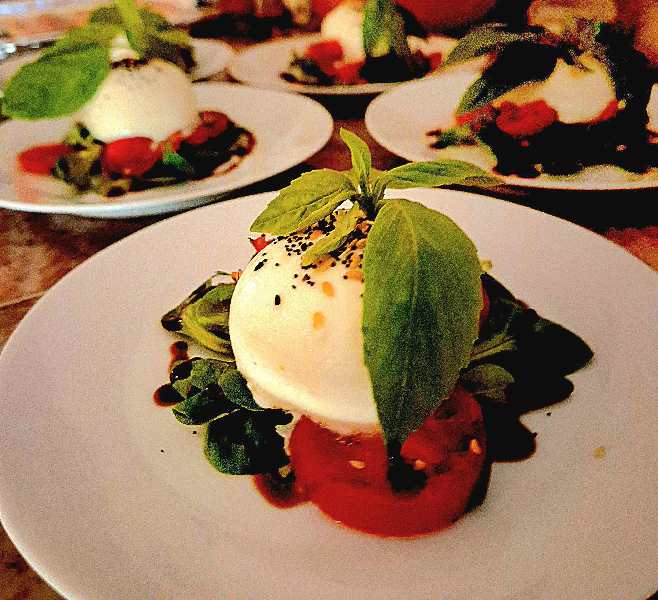 Caprese salad with burrata cheese, tomatoes, spinach, basil, and balsamic glaze on white plates.