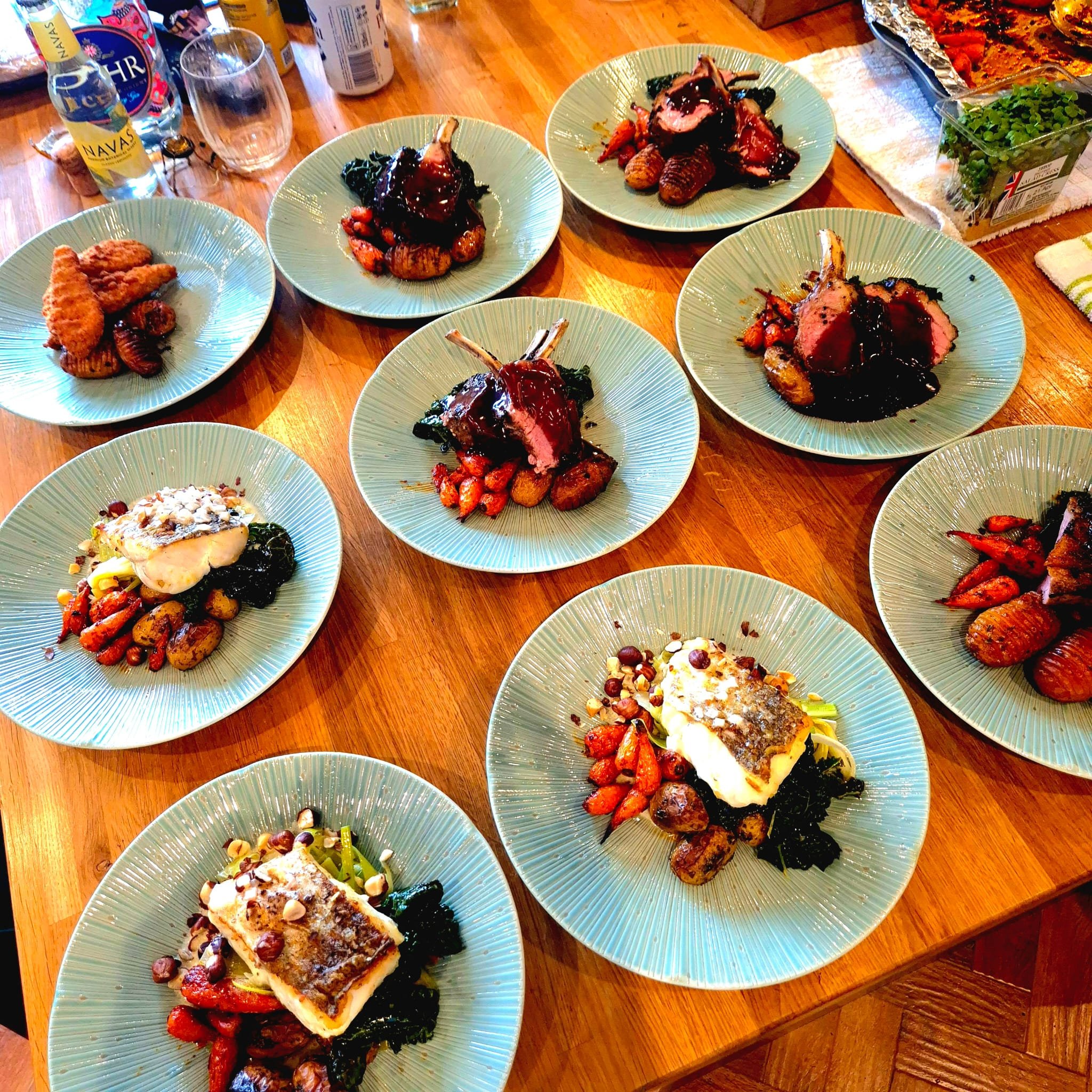 Multiple plates with prepared meat dishes, vegetables, and garnishes on a wooden table, likely for a meal or dinner.