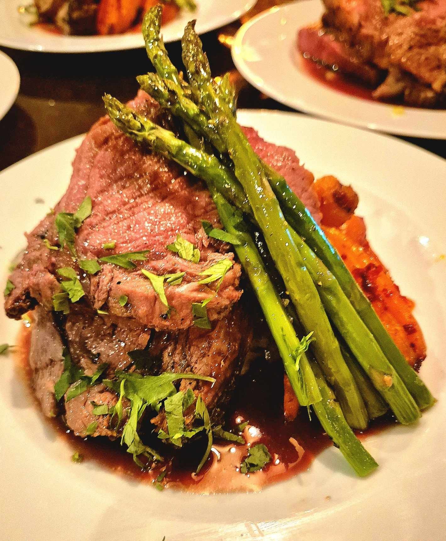 Plate with roasted beef, asparagus, and herbs, served with a sauce.