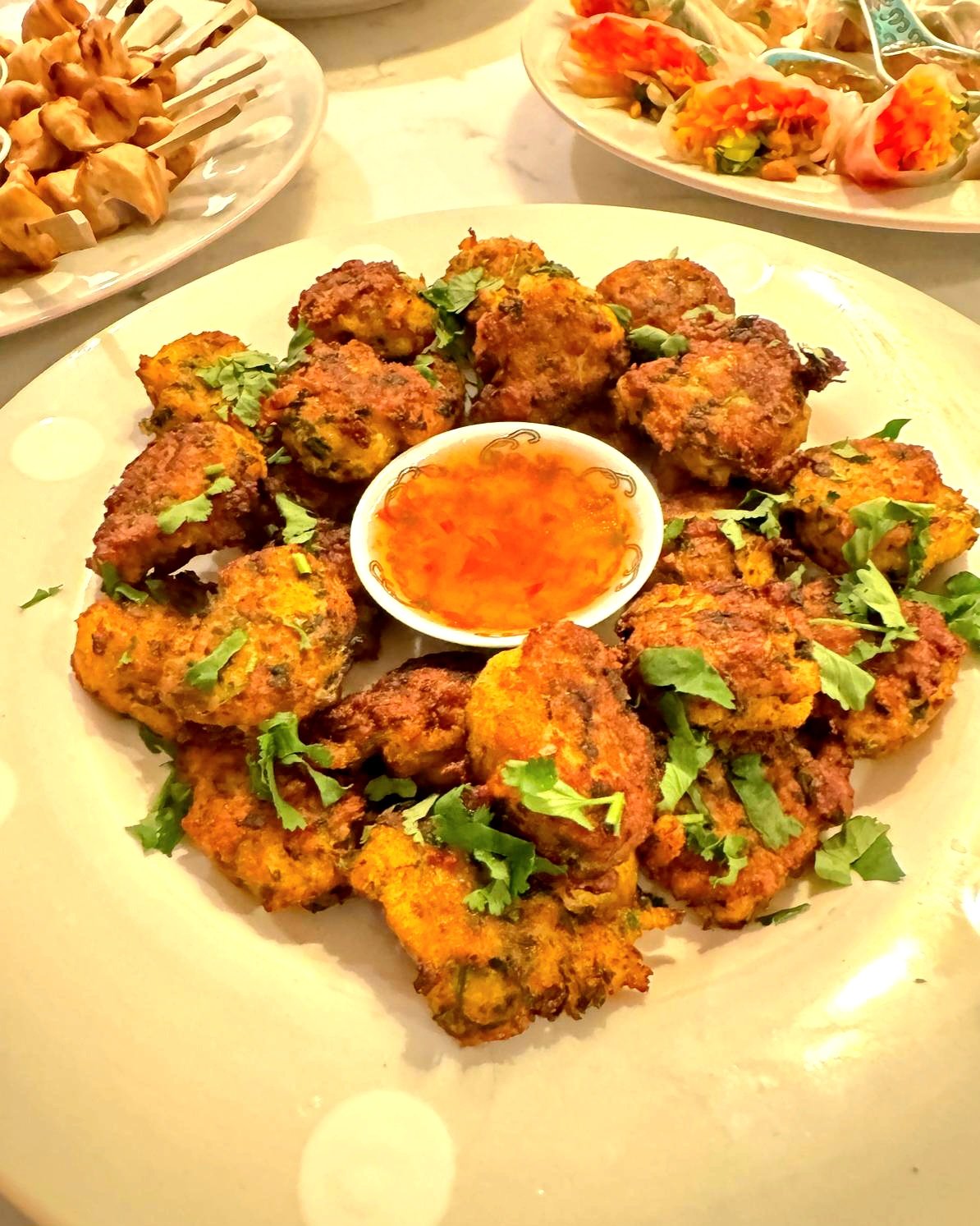 Plate of fried fritters garnished with cilantro, centered around a small bowl of orange dipping sauce.