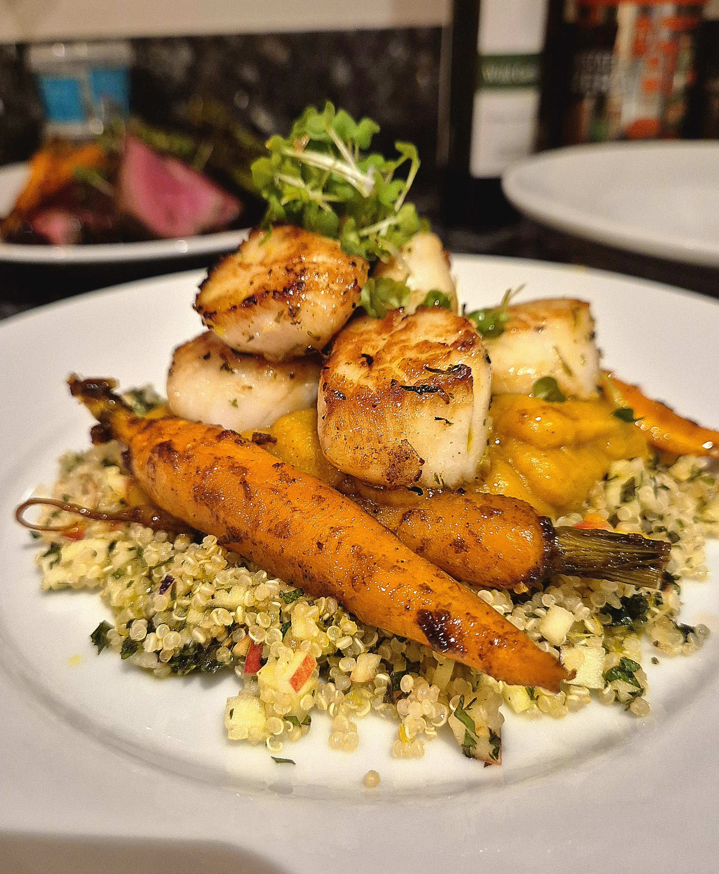 Grilled scallops with roasted carrots on quinoa salad garnished with microgreens on a white plate.