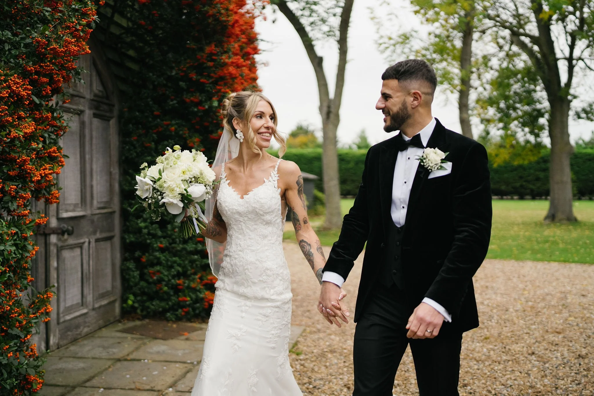 A bride and groom holding hands and walking across a grassy field with a rainbow in the background.