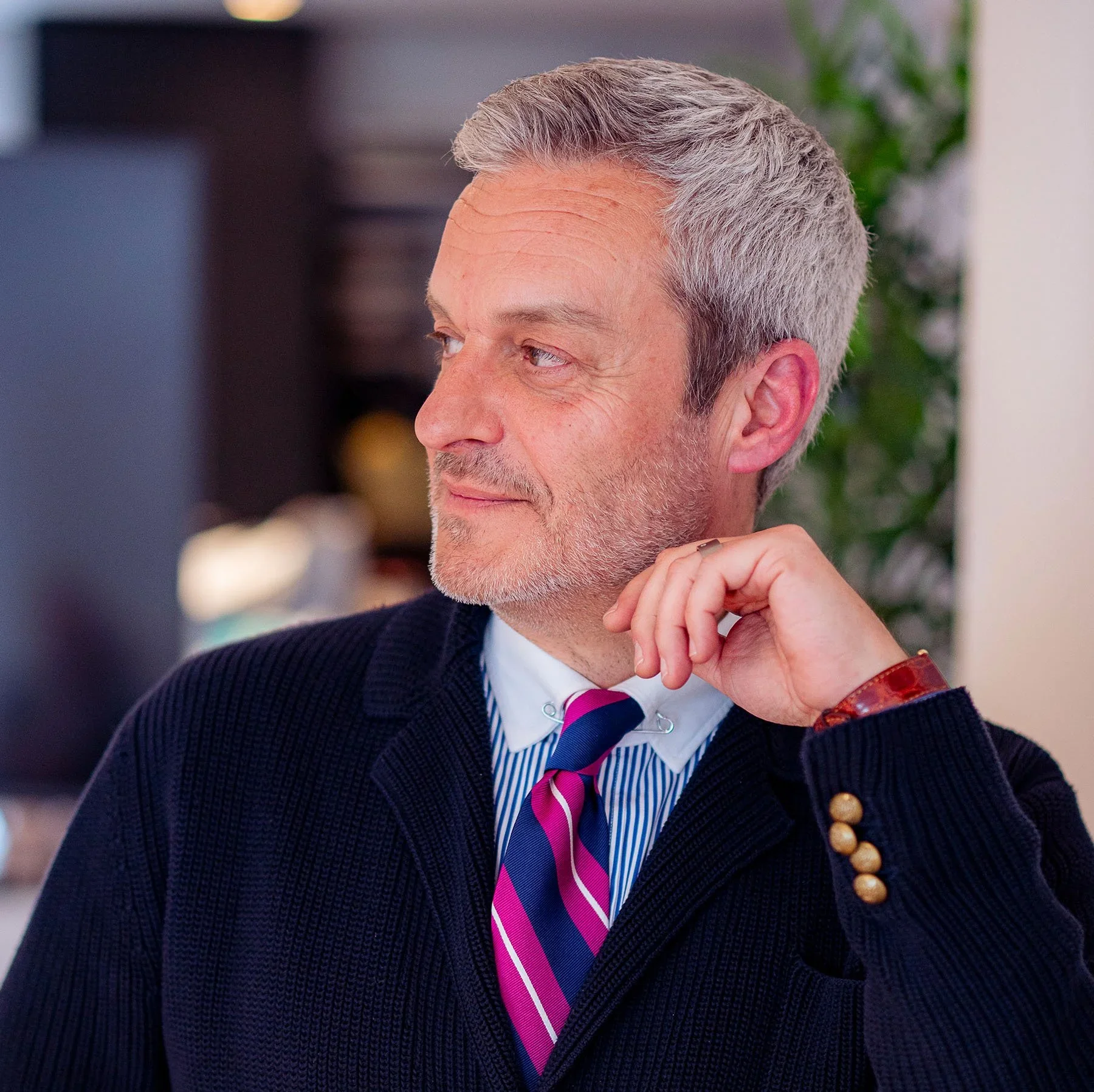 Mark Nunez in a navy cardigan and pink striped tie looking to the side in a portrait.