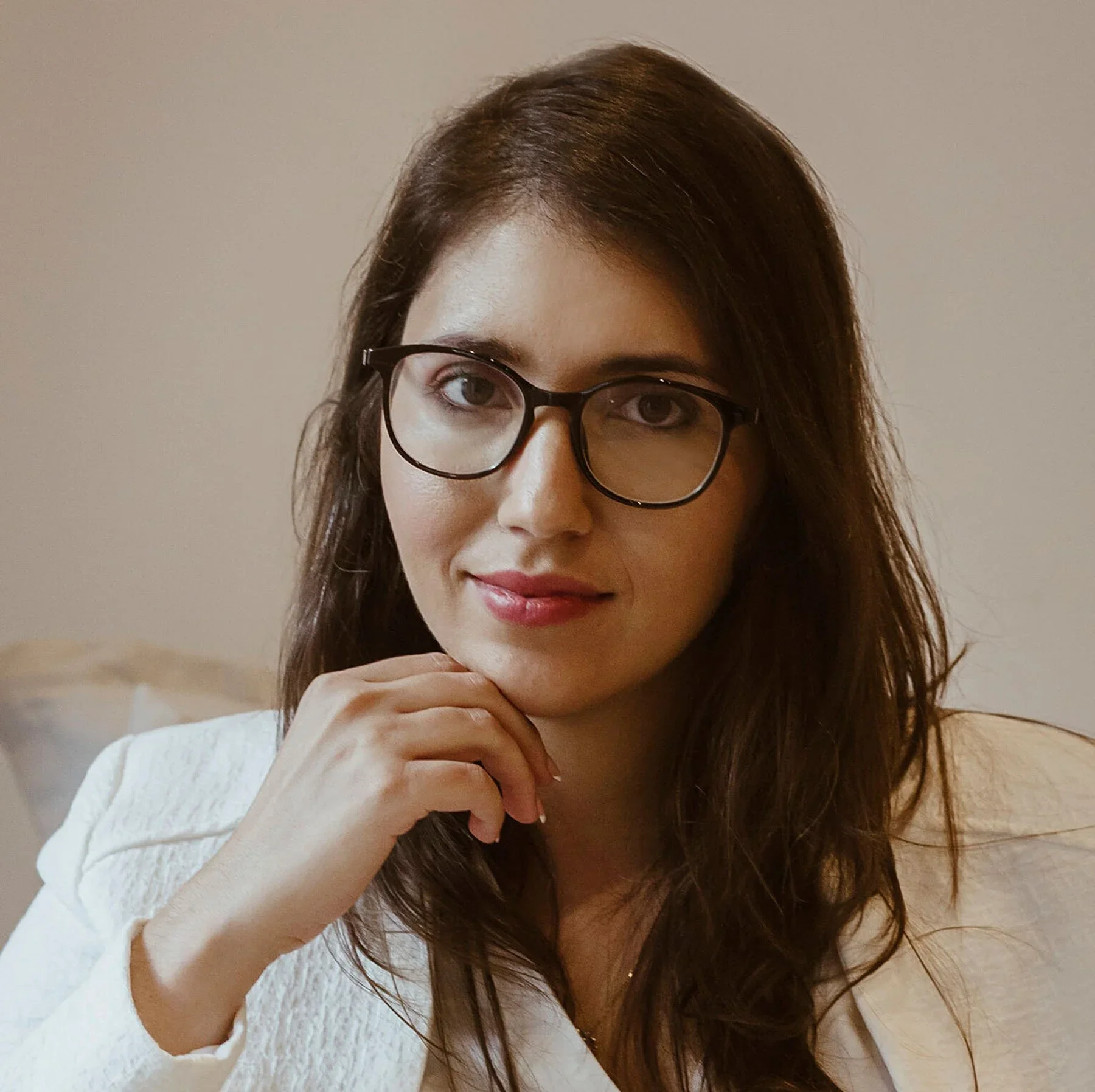 Paty Soares wearing glasses and a white blazer in a studio style headshot.