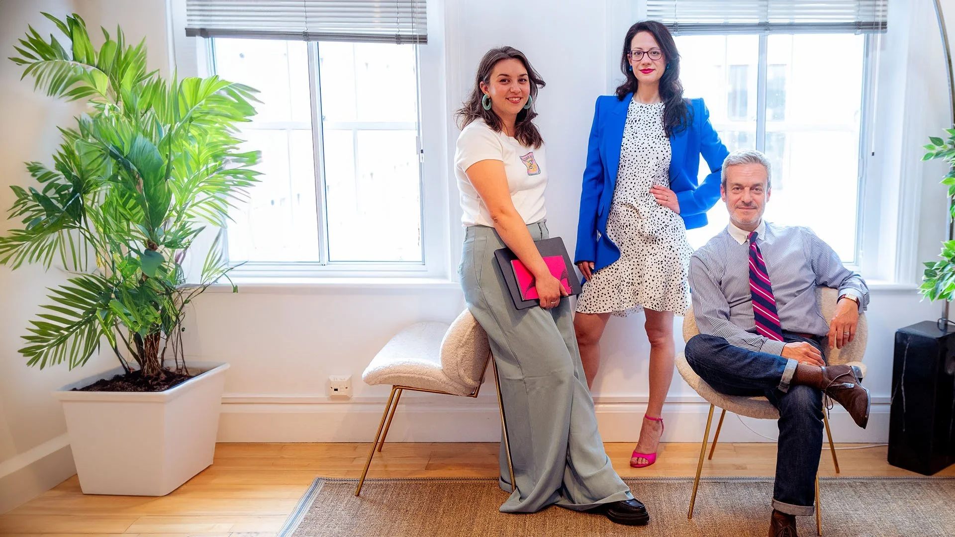 Three Saia Creative team members posing in a bright office space with large windows and plants.
