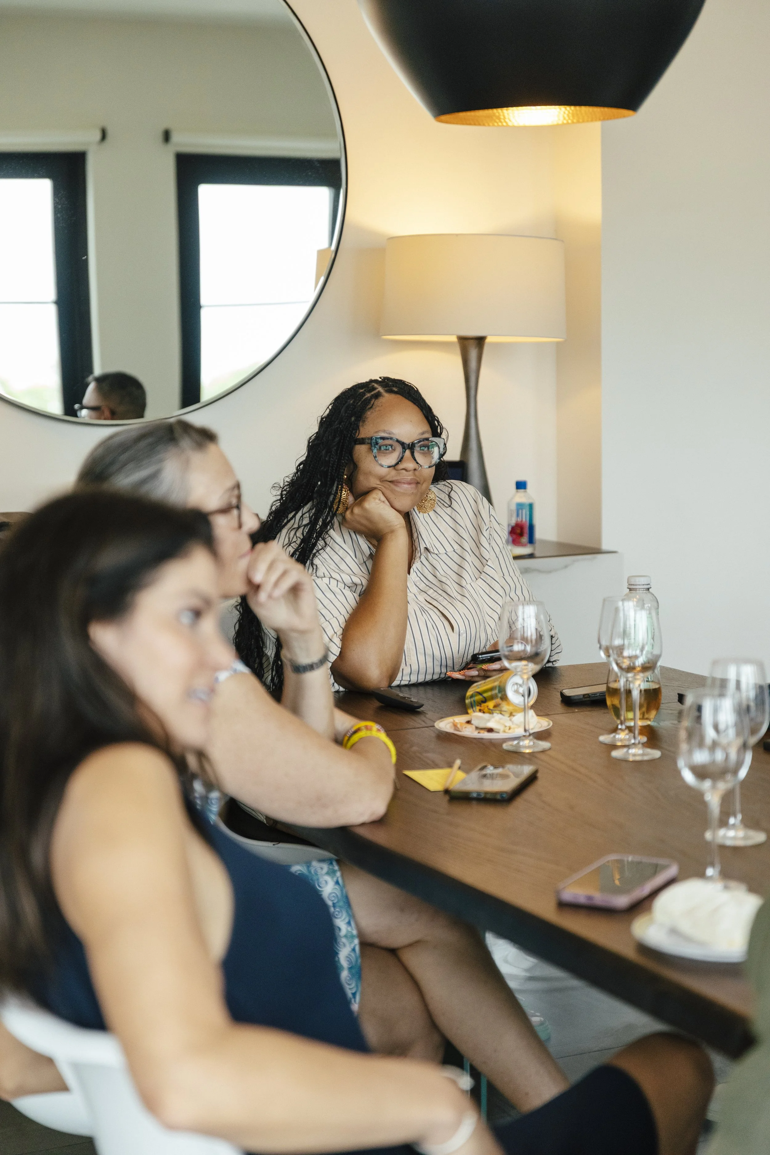 Woman with black hair and glasses writing listening at a conference or meeting.