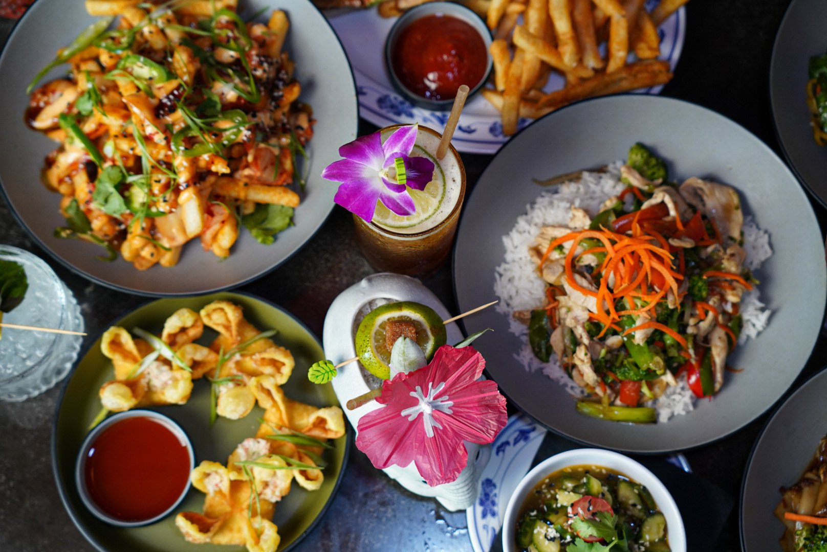 Overhead view of a plated rice bowl topped with vegetables and protein, served alongside a tropical cocktail with a flower garnish.