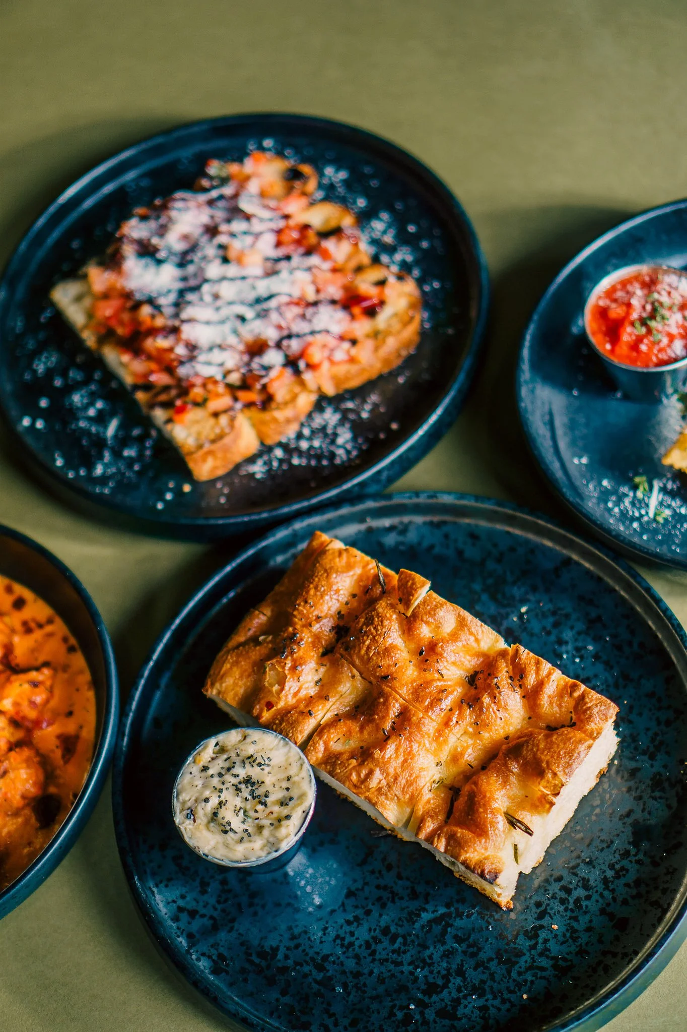 Plated focaccia-style bread with herb butter alongside small plates and dips, photographed on a restaurant table at Orange Umbrella Restaurants.