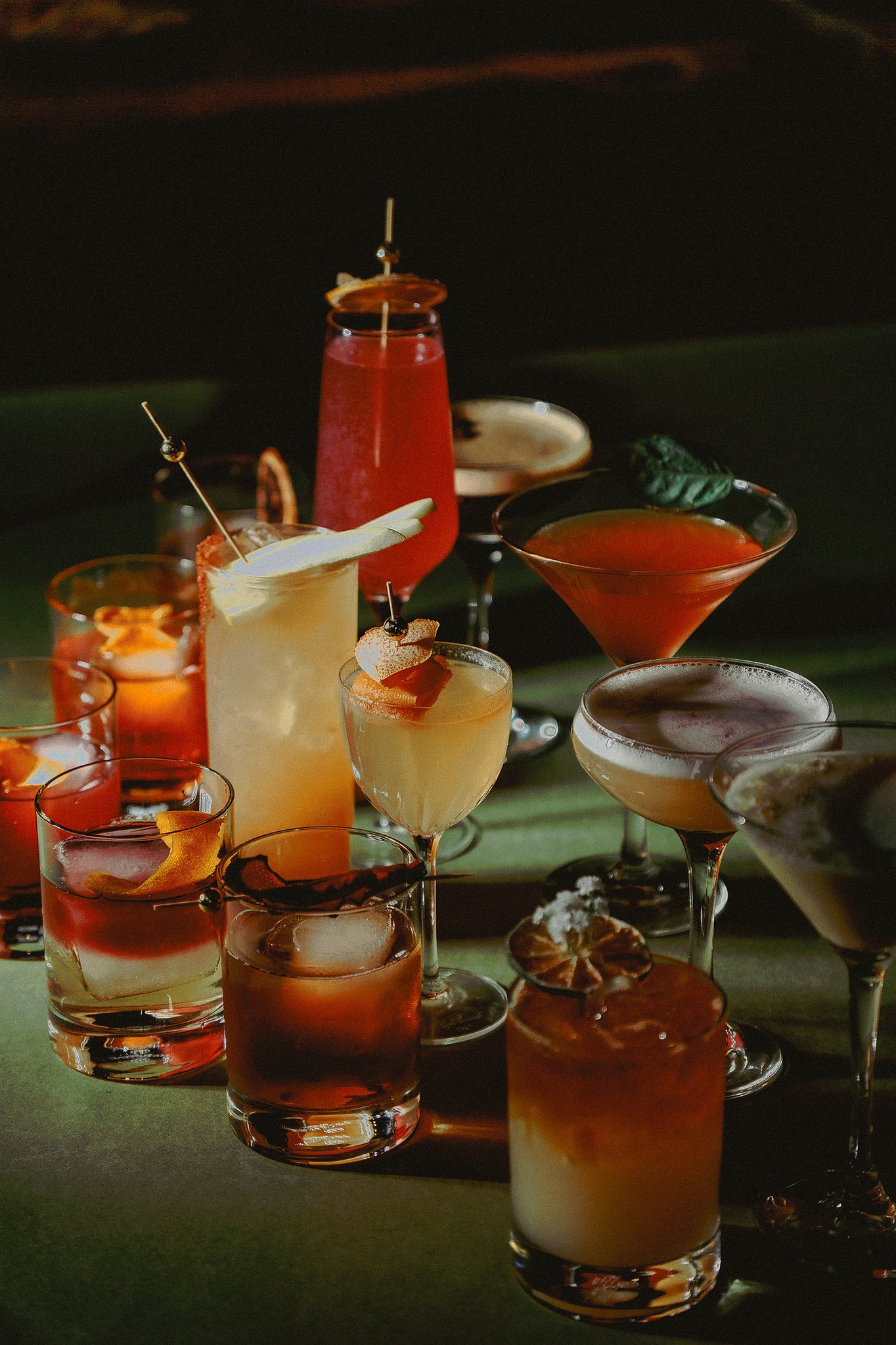 A selection of handcrafted cocktails on a table, featuring martinis, old fashioneds, and festive drinks in a dimly lit bar setting.