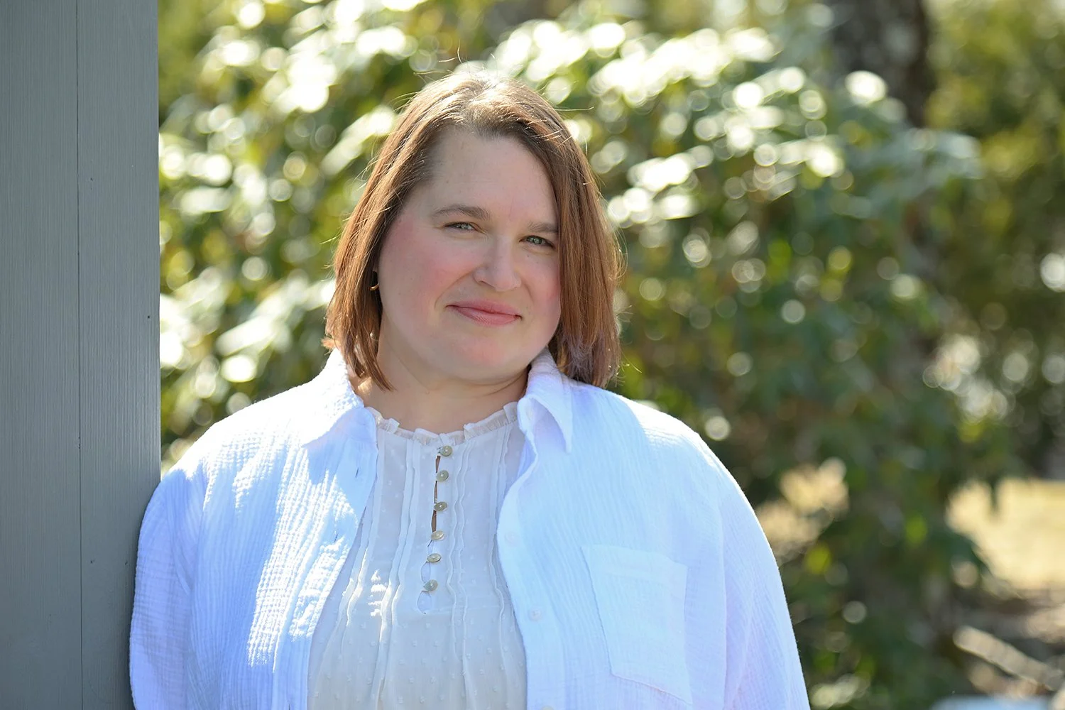 Alison wearing white shirts in front of trees, inviting you to contact her