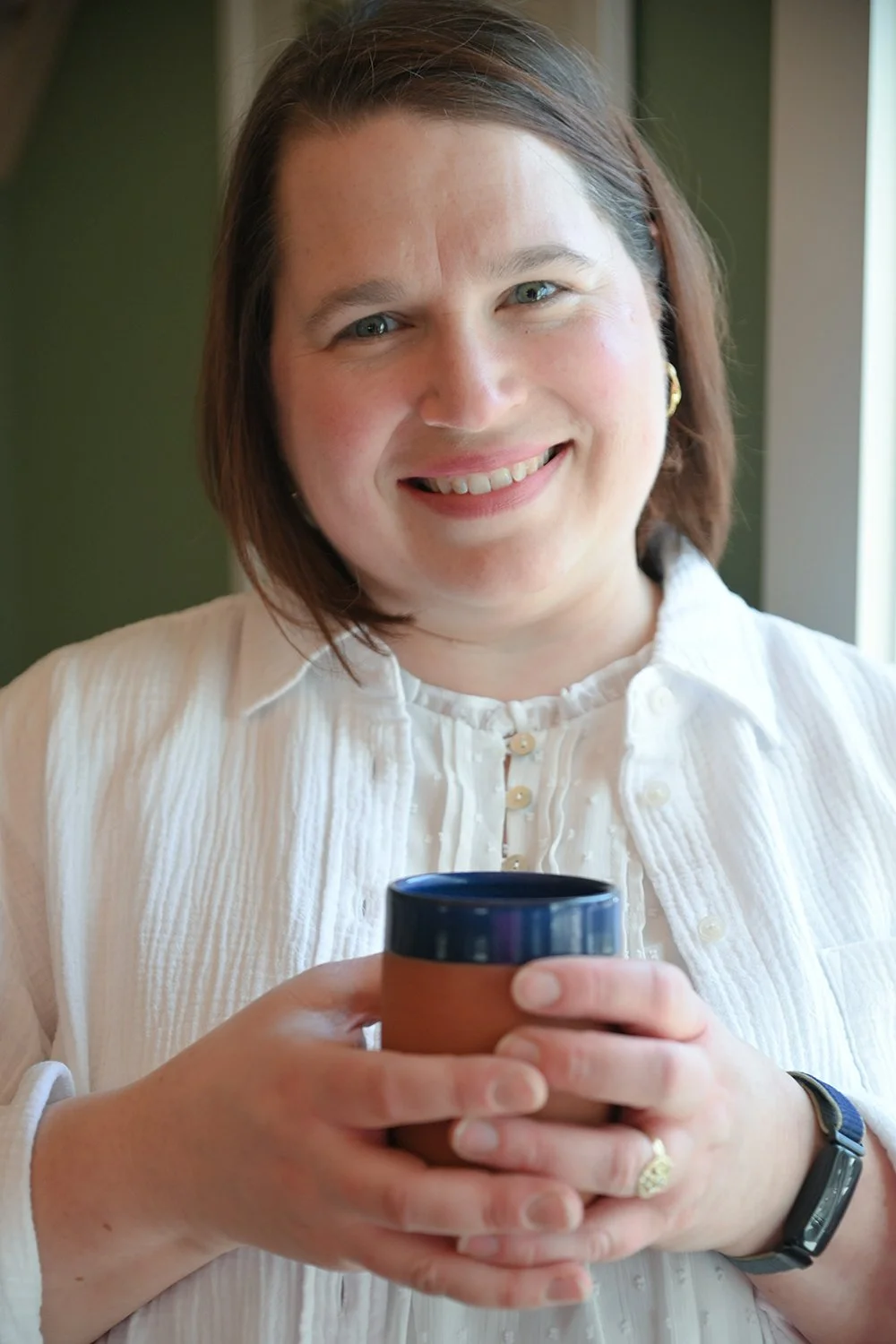 Alison Keller, death doula in Easthampton, MA, holding a mug, smiling at the camera