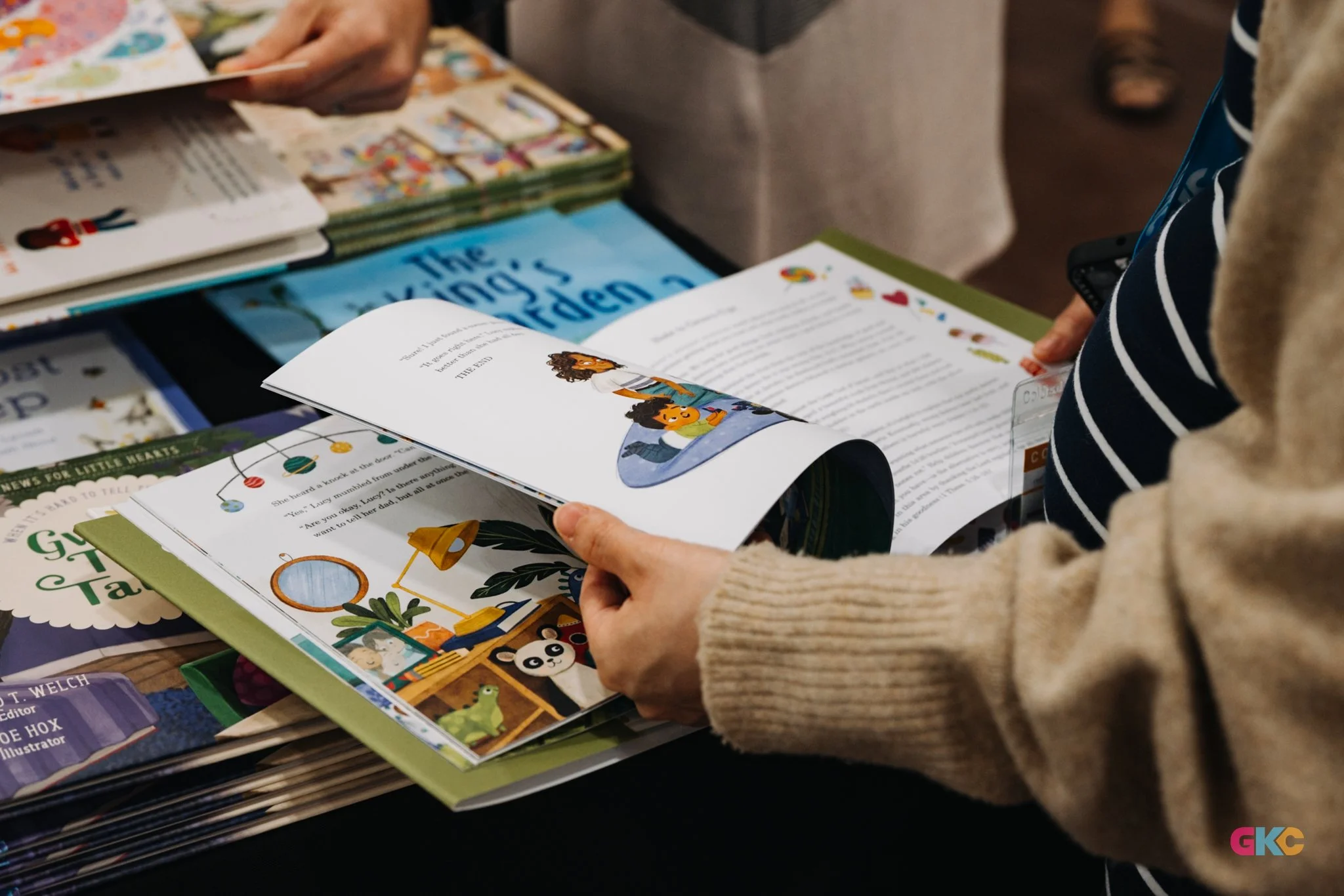 Person flipping through a children's book at a table with various other books around.