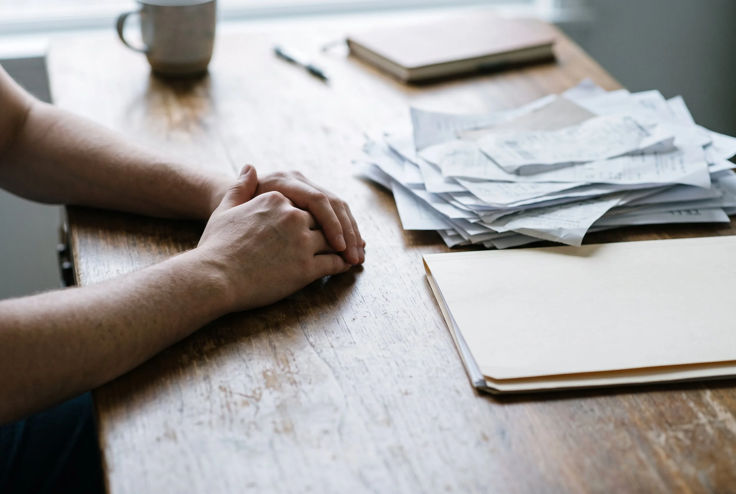 Hands resting on a desk beside a messy paper pile and one sorted folder